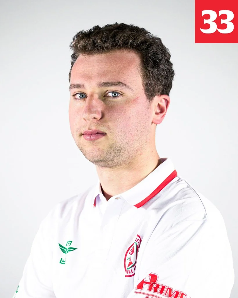 Young man with short, dark hair and blue eyes wearing a white sports jersey with red and green accents, and the number 33 in white on a red background in the top right corner.