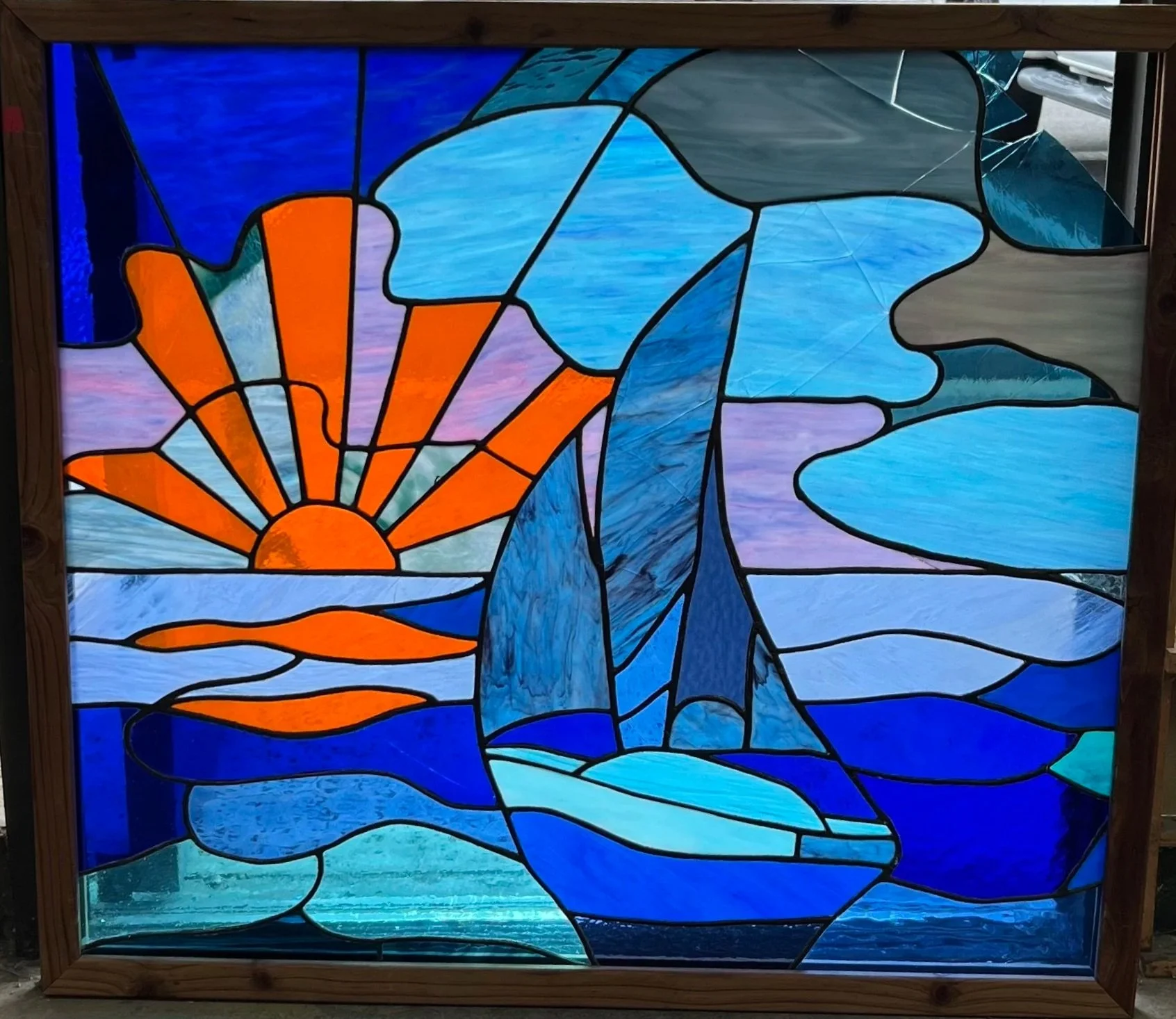 Colorful stained glass window depicting a sunset over water with clouds and blue sky.