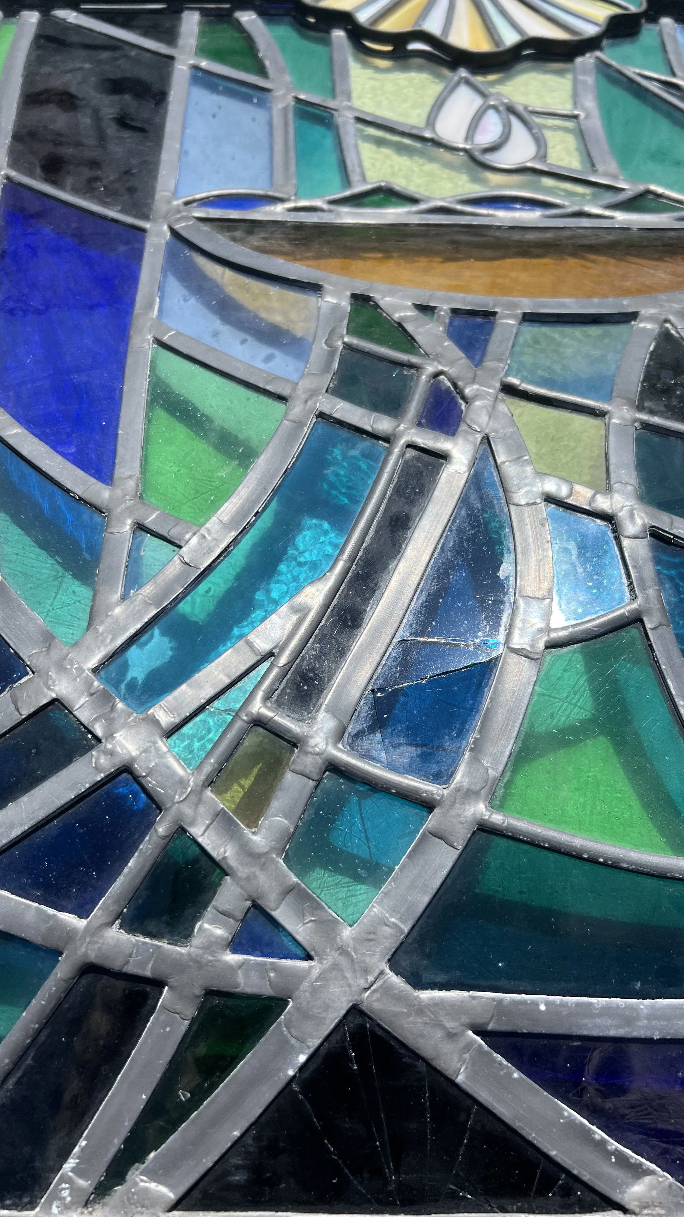 Close-up of stained glass repair with various colored glass pieces held together by metal framework.