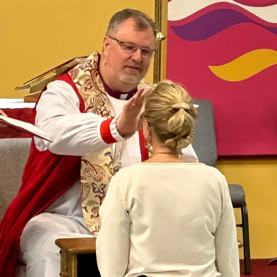 Bishop Alan Hawkins places his hand on a kneeling woman's head as he confirms her at Christ the Redeemer Anglican Church, Norfolk, VA