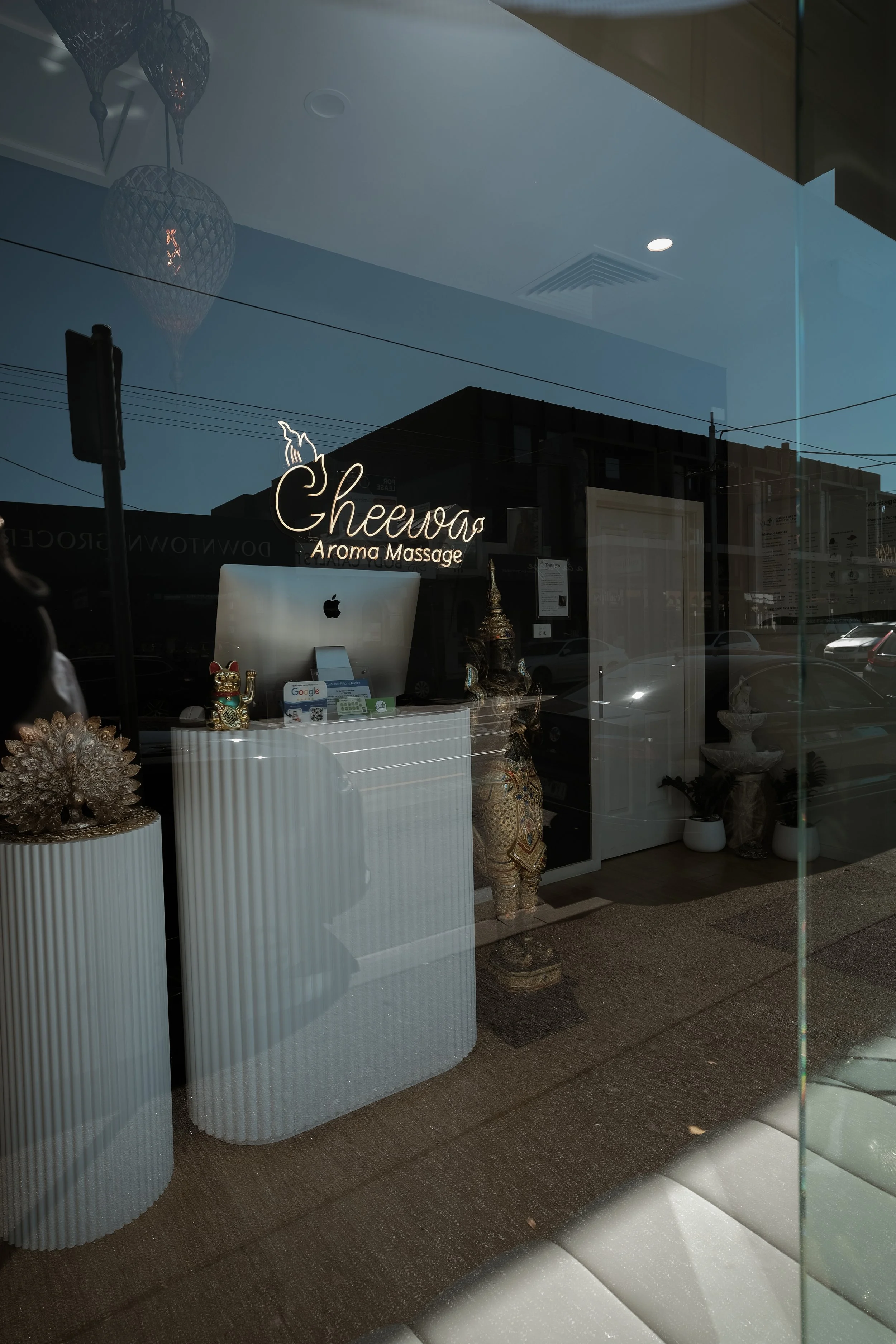 The window display of Cheewa Aroma Massage shop with decorative statues and a computer.