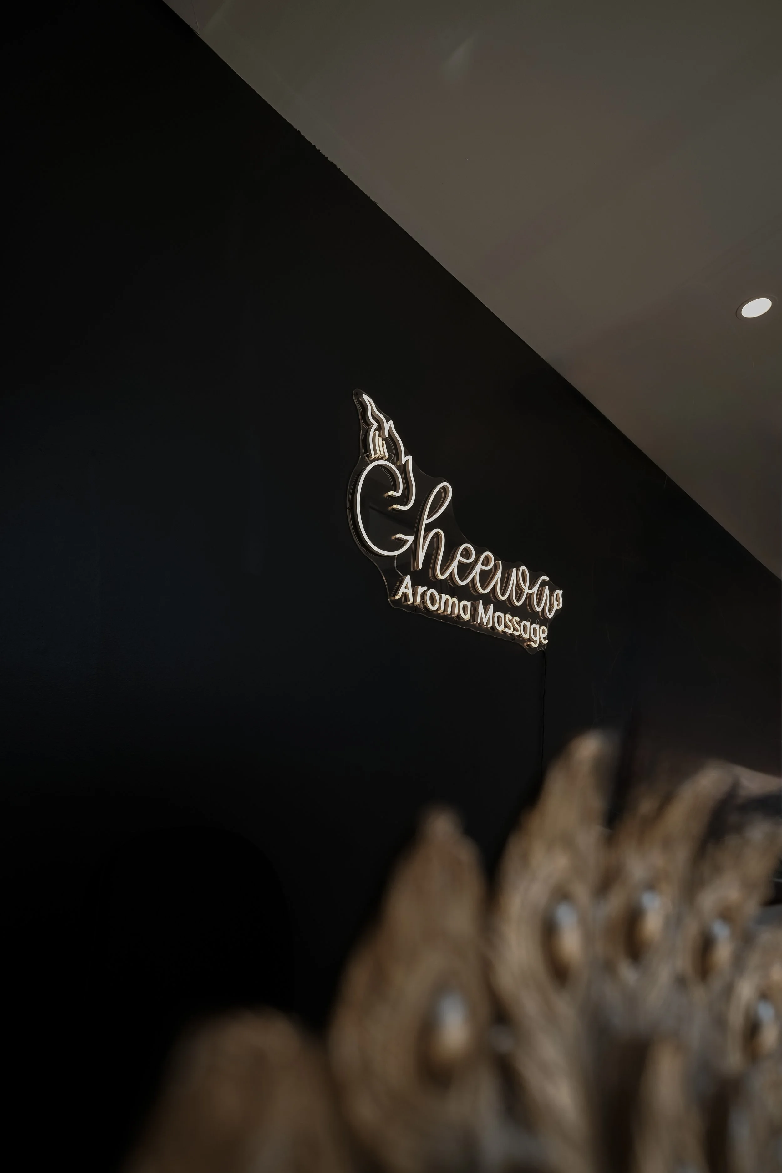 Sign that says 'Chewa Aroma Remedial Massage' with a decorative flame, mounted on a dark wall ceiling