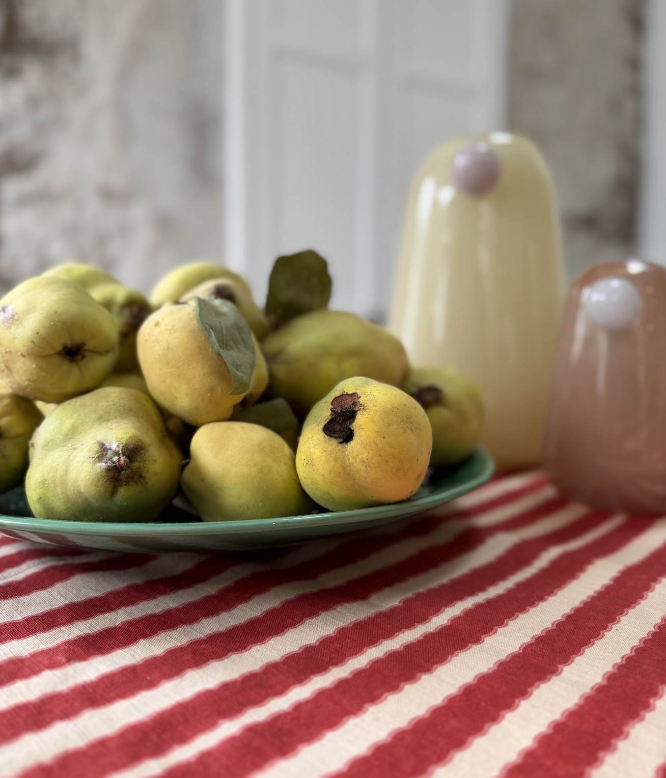 A plate of ripening guavas on a red and white striped tablecloth, with ceramic salt and pepper shakers in the background.