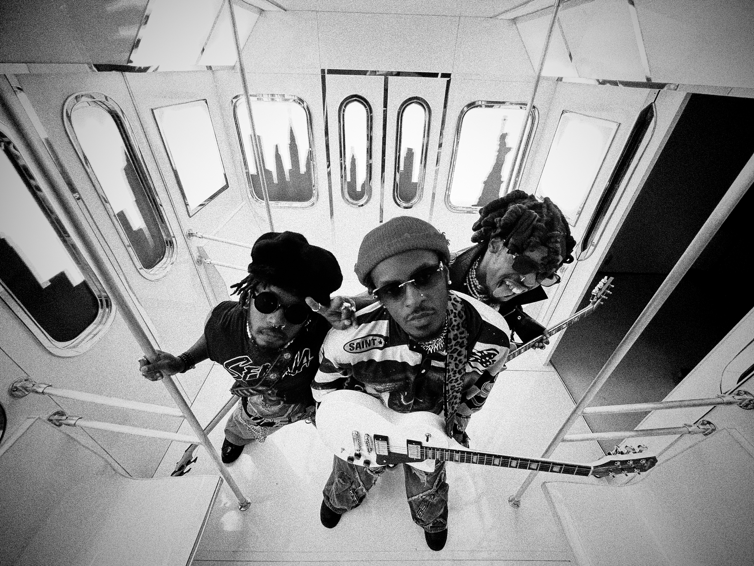 Three people taking a selfie in an elevator with a cityscape visible through the windows behind them.