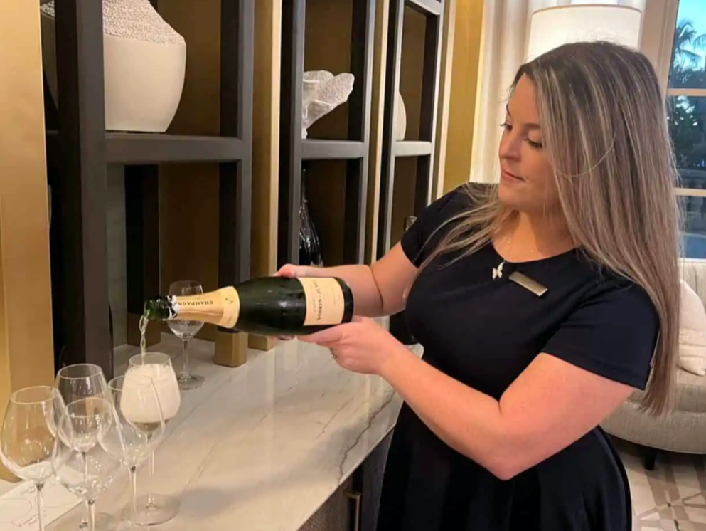 A woman pouring champagne into glasses on a marble counter.