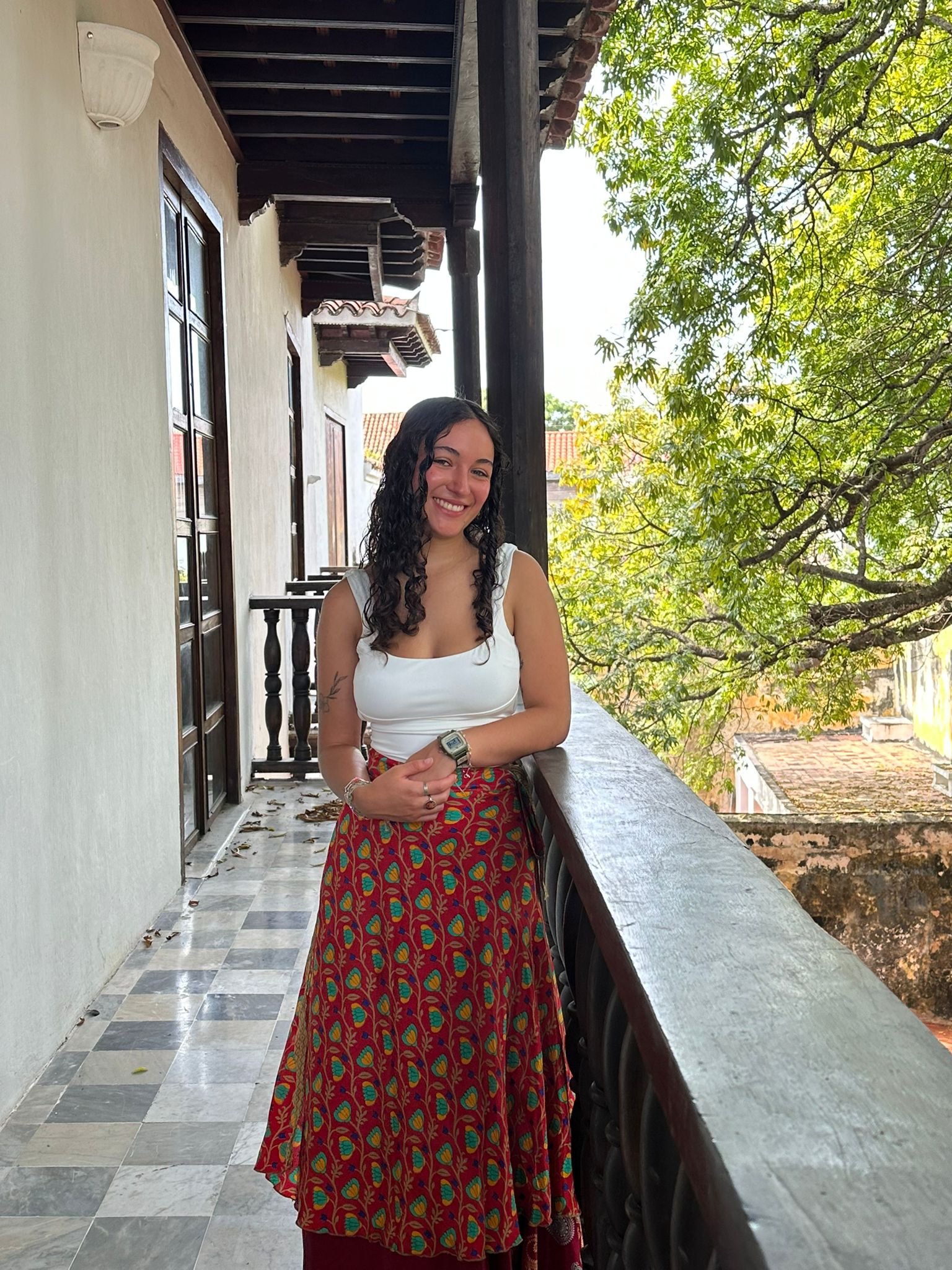 Smiling woman with brown curly hair on a balcony resting her arm on the railing.
