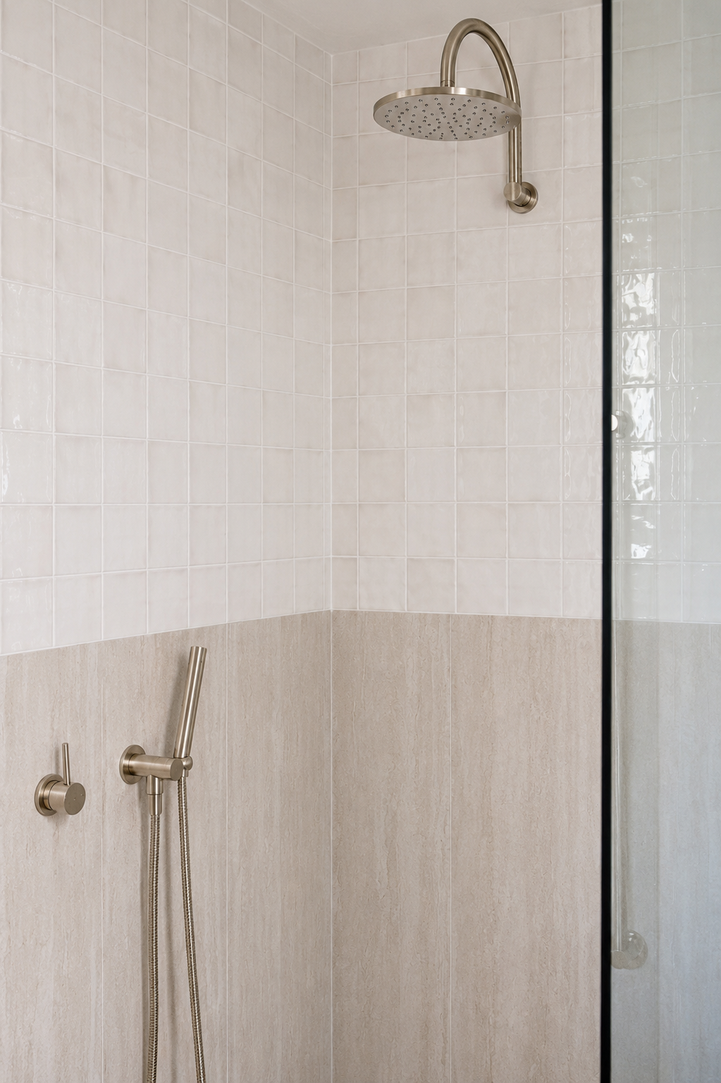 A modern shower area with a large round rain showerhead mounted on the ceiling, a handheld shower with a hose, and a partial glass shower partition. The walls are tiled with light beige and cream-colored tiles.