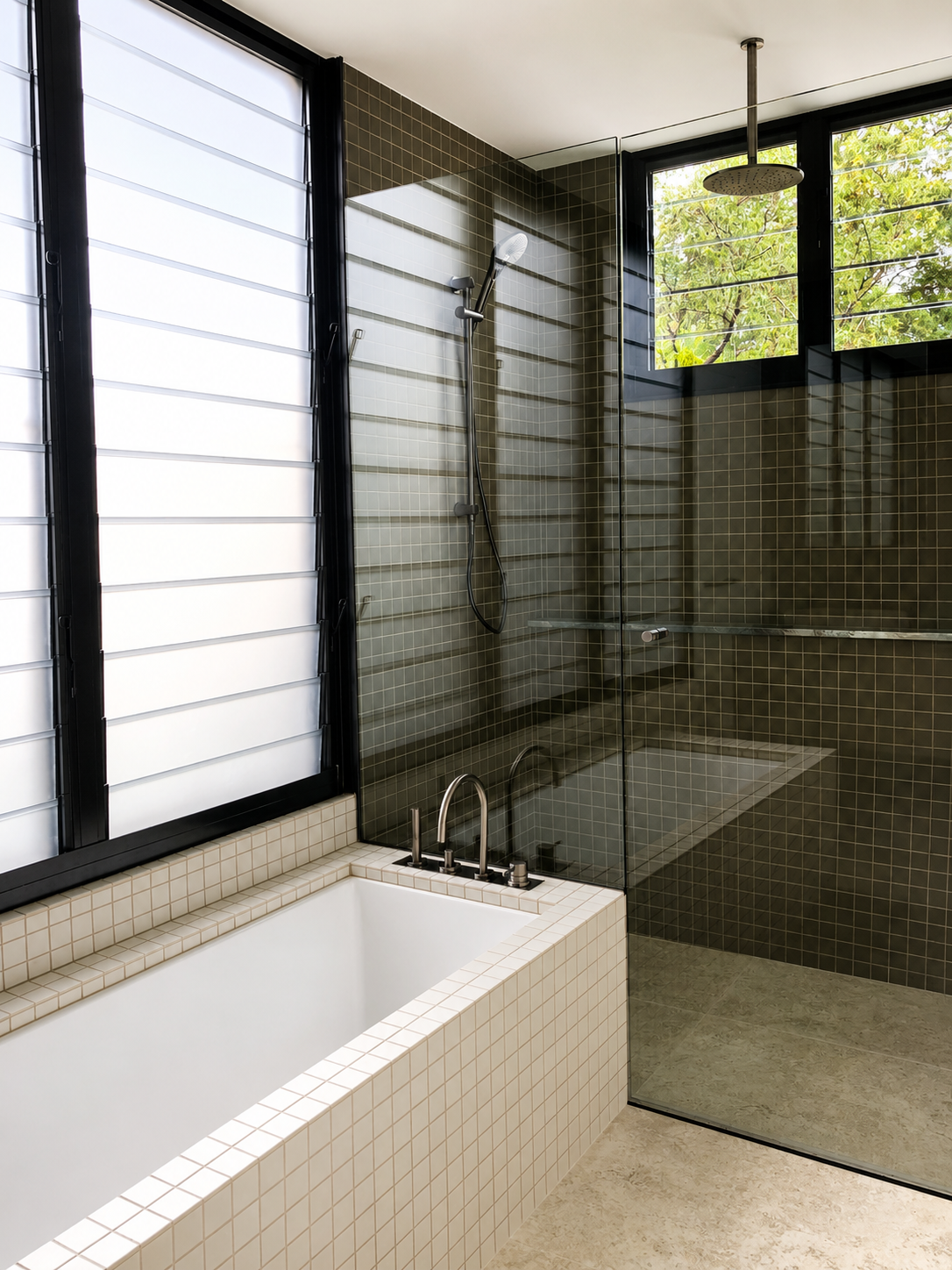 Modern bathroom with bathtub and a glass-enclosed shower, large windows with shutters, green outdoor view, beige tiled floor, and dark brown tiled walls.