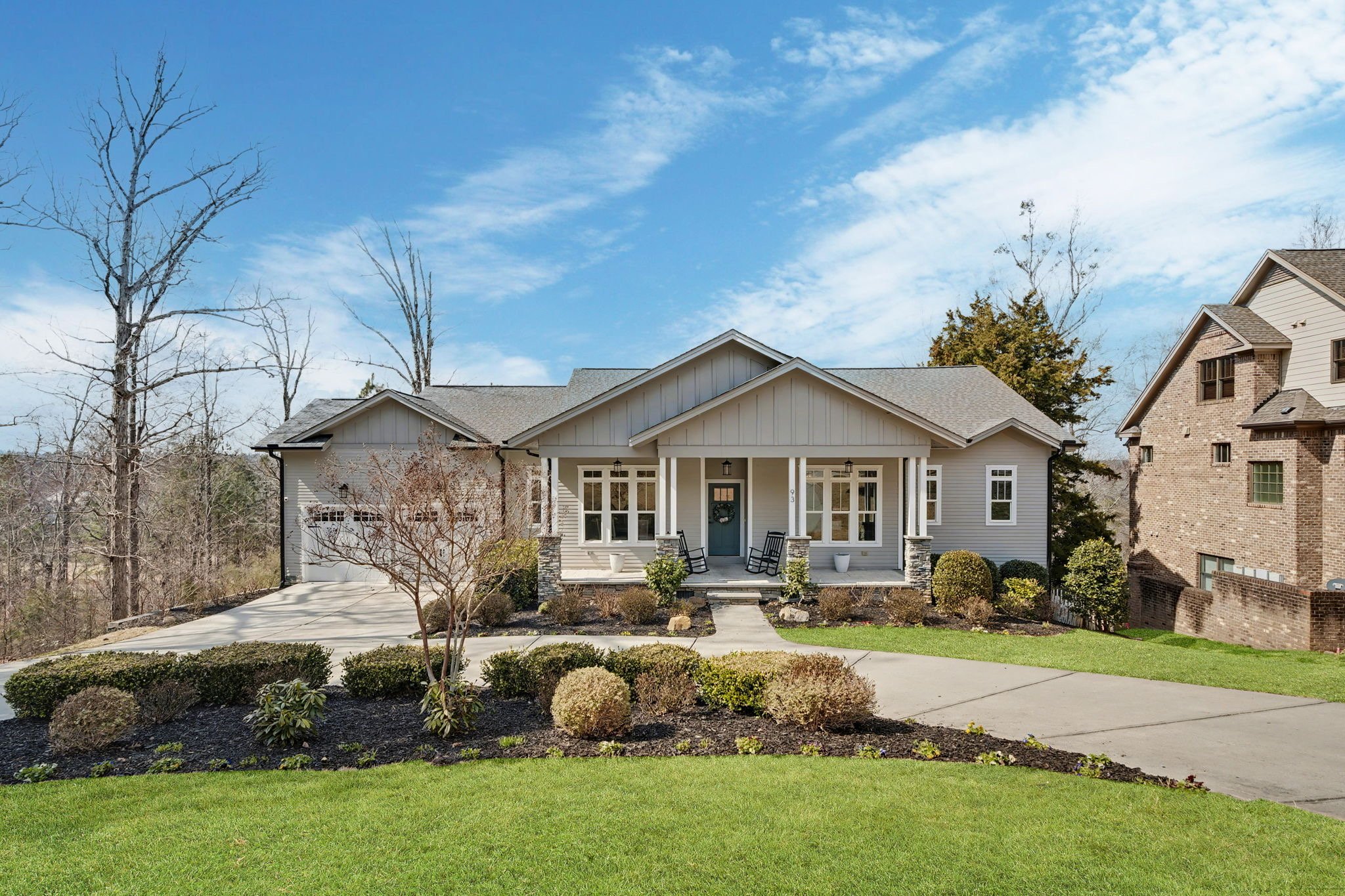Grey single story home with a curved driveway across the front, with a two car garage on the left and. a blue front door in the center.