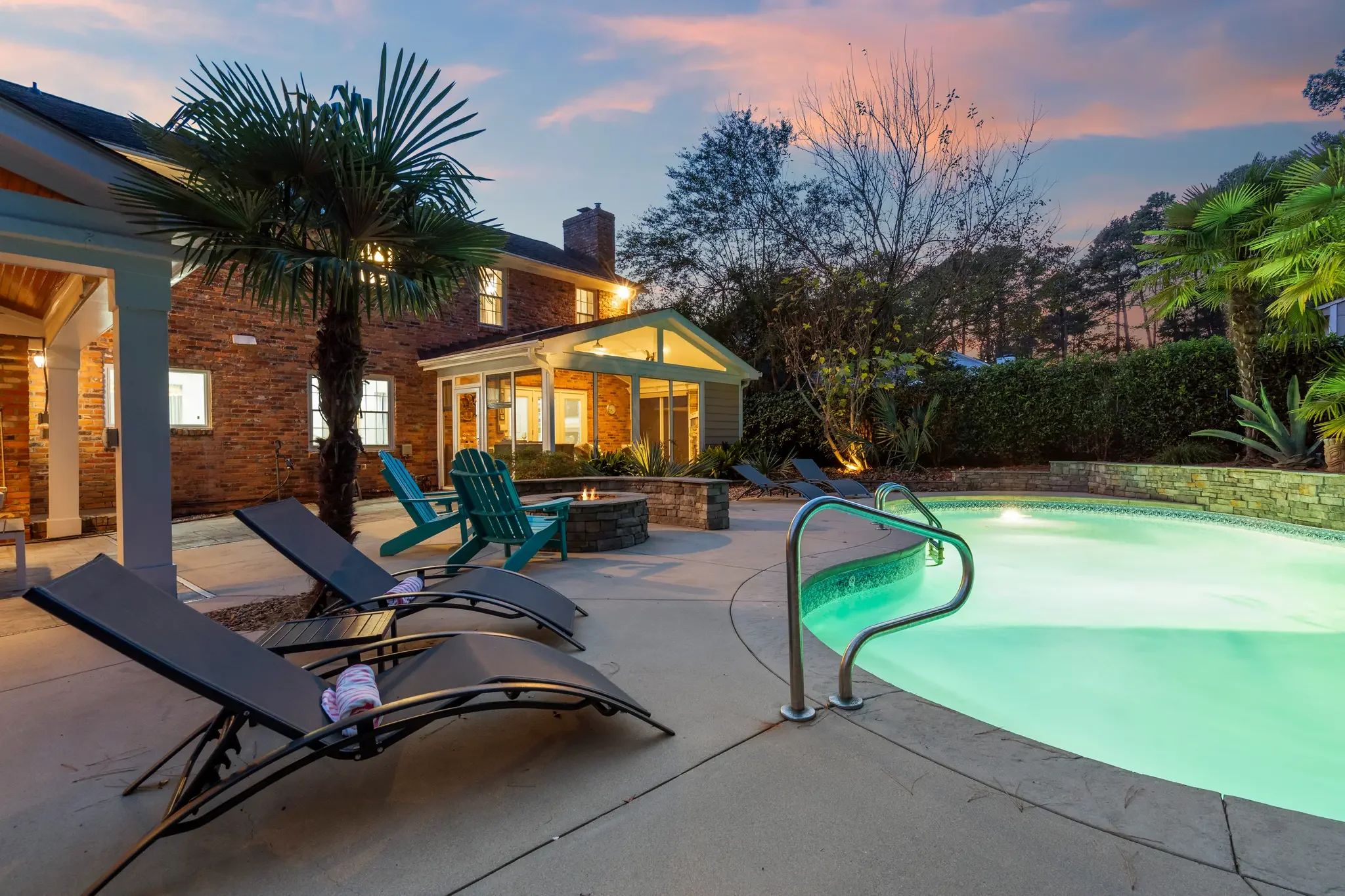 Back of house overlooking a pool and pool lounge chairs during sunset.