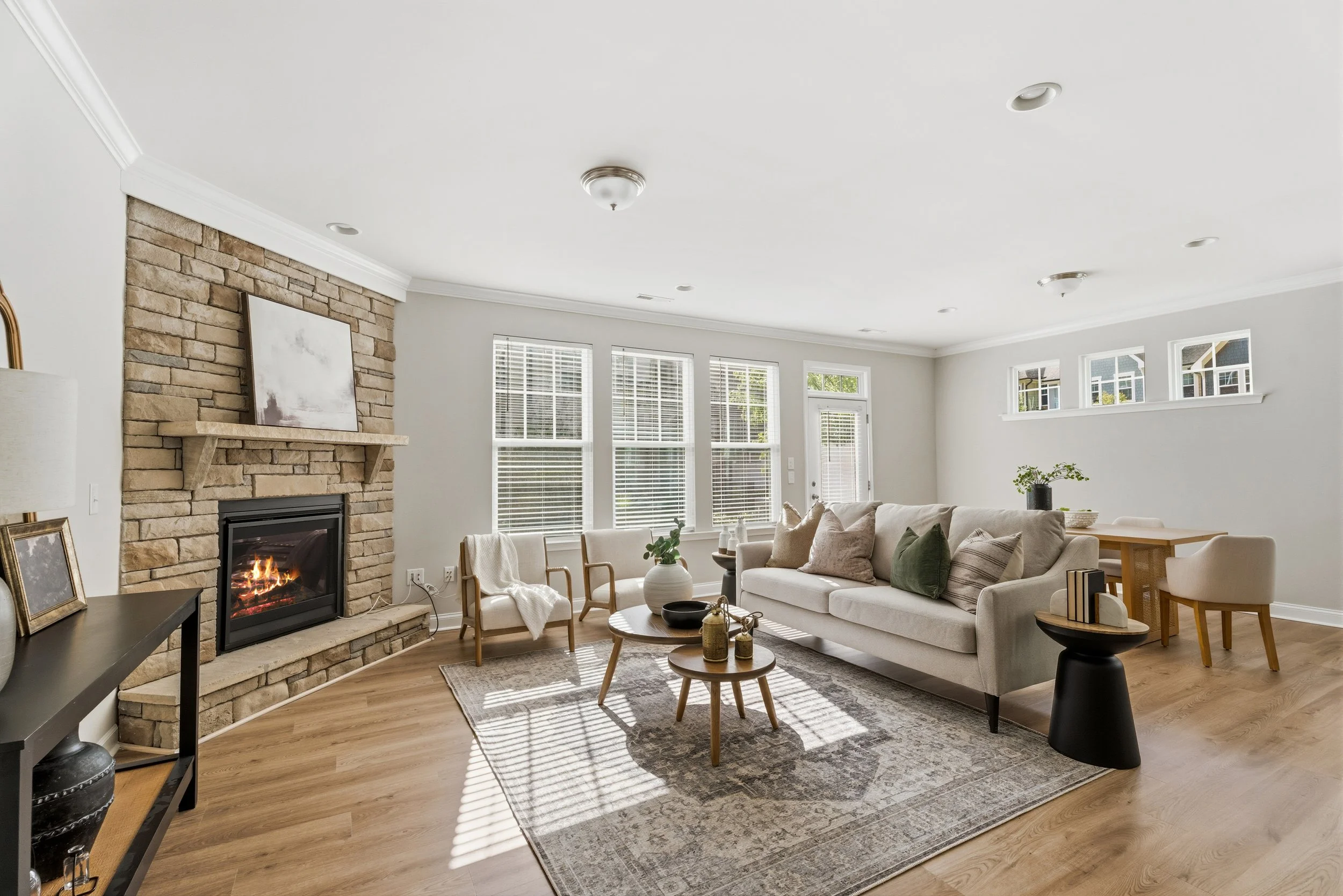 Dining room with a rectangular marble table, six green velvet chairs with gold accents, a vase with orange flowers, a hanging glass bubble chandelier, three framed floral pictures on a blue accent wall, a gold-framed mirror on a white wall, and a door with a window and blinds.