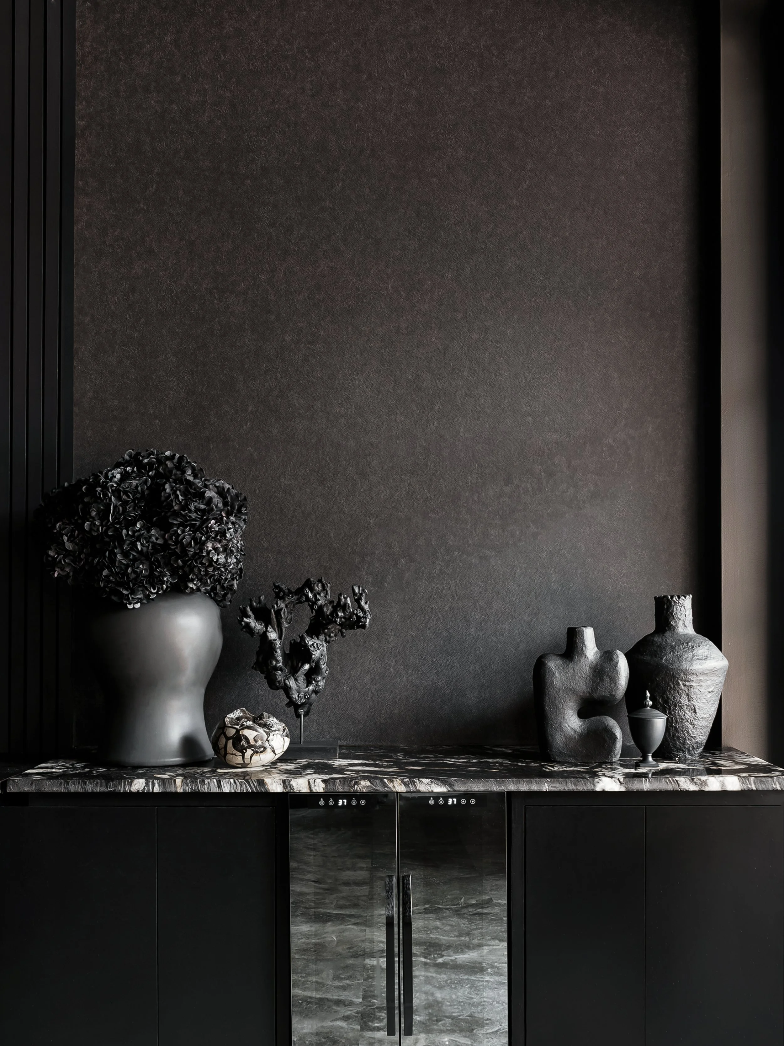 Black beverage bar with all black plant pots, small sculptures, and a dragon egg.