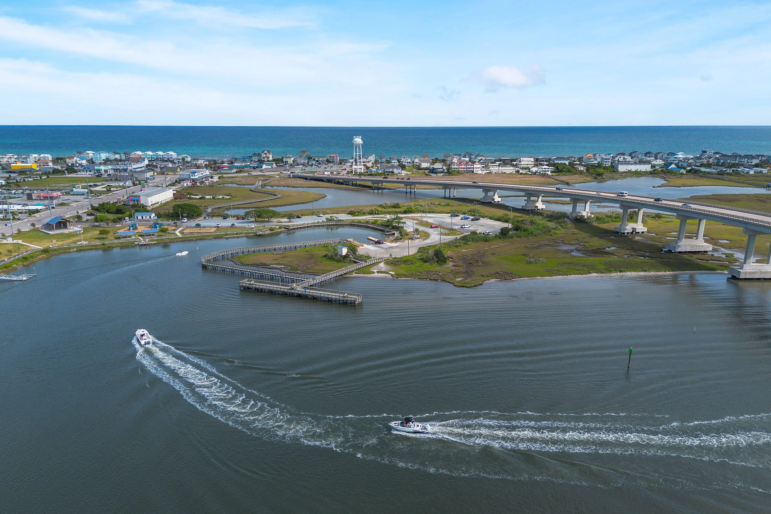 Boats at the beach in the water with the topsail island bridge to surf city in the background. Contains the surf city water tower.