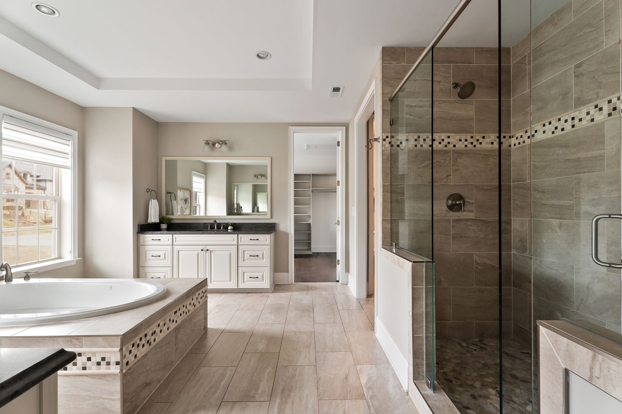 Large cream colored bathroom with a glass shower on the right, a large jacuzzi tub on the left, and a closet and counter in the back. 