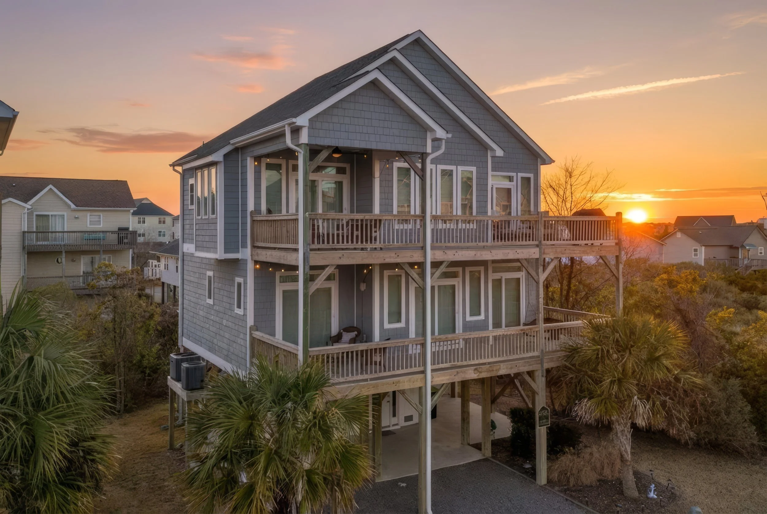 Front of a 2 story beach house against. a sunset background.