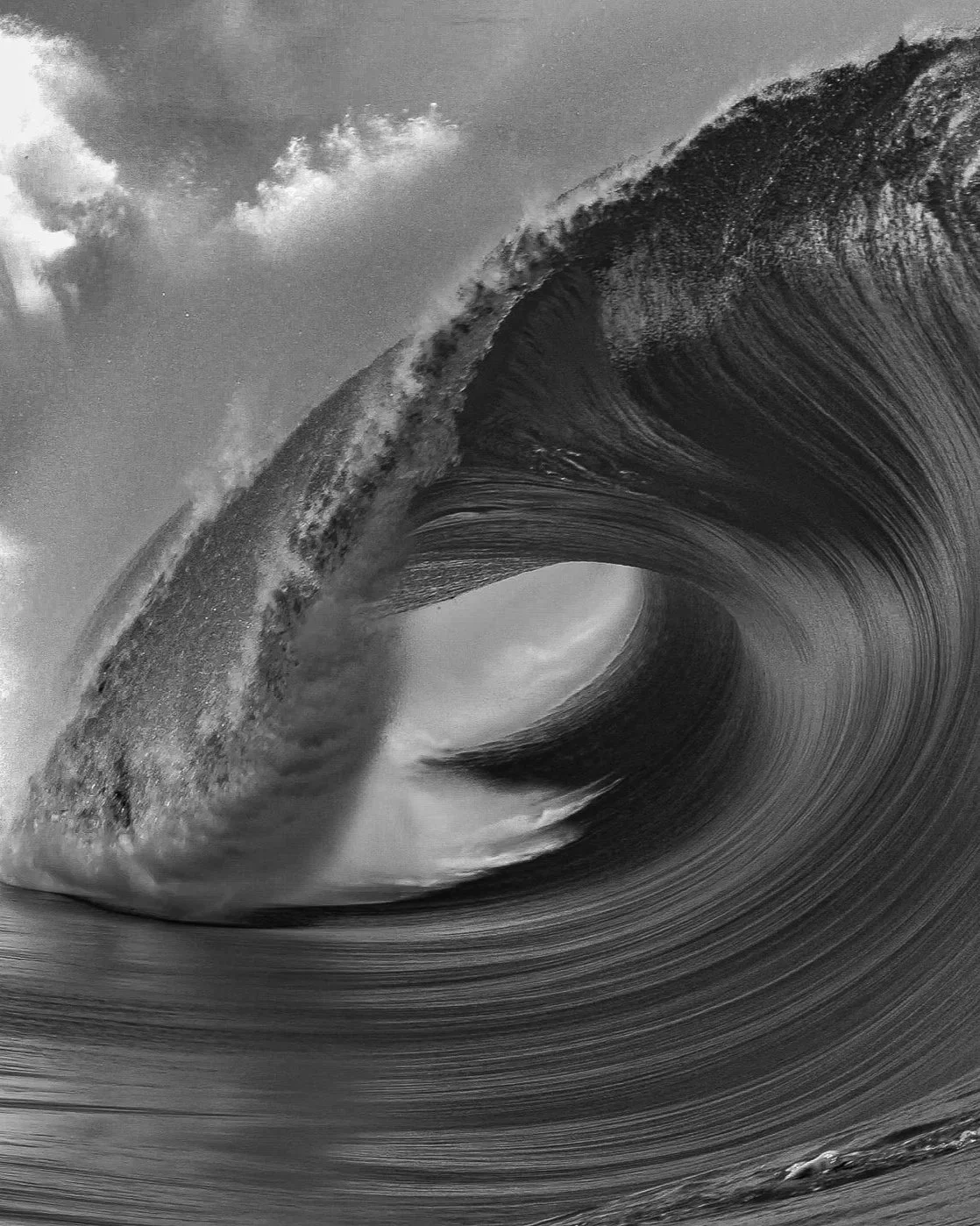 Black and white photograph of a large ocean wave curling over, with some clouds visible in the sky.