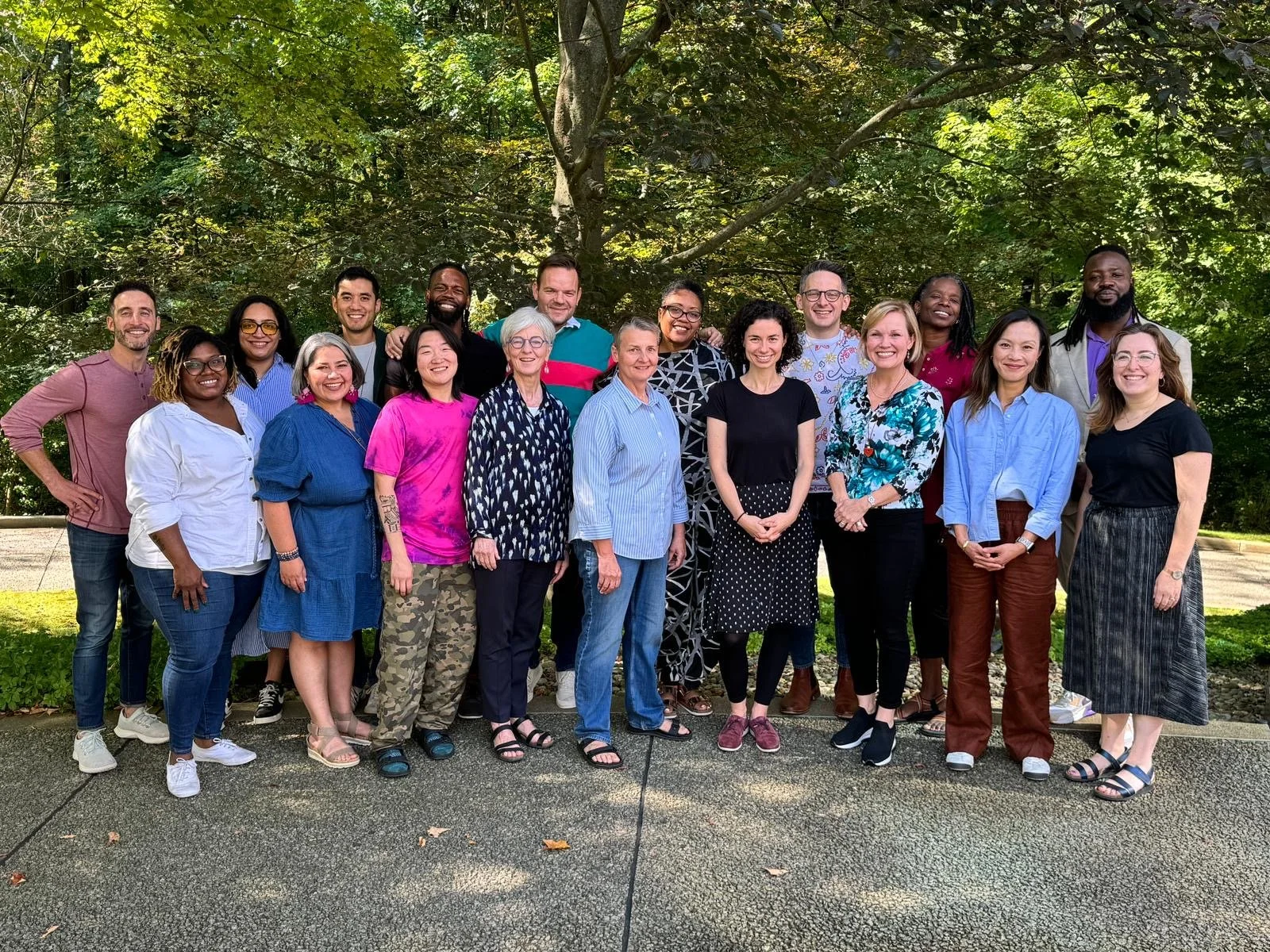 Group of diverse people smiling outdoors with lush greenery in the background.