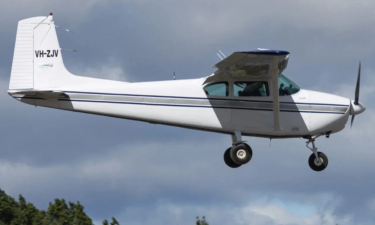 A small aircraft flying through the sky with clouds in the background.