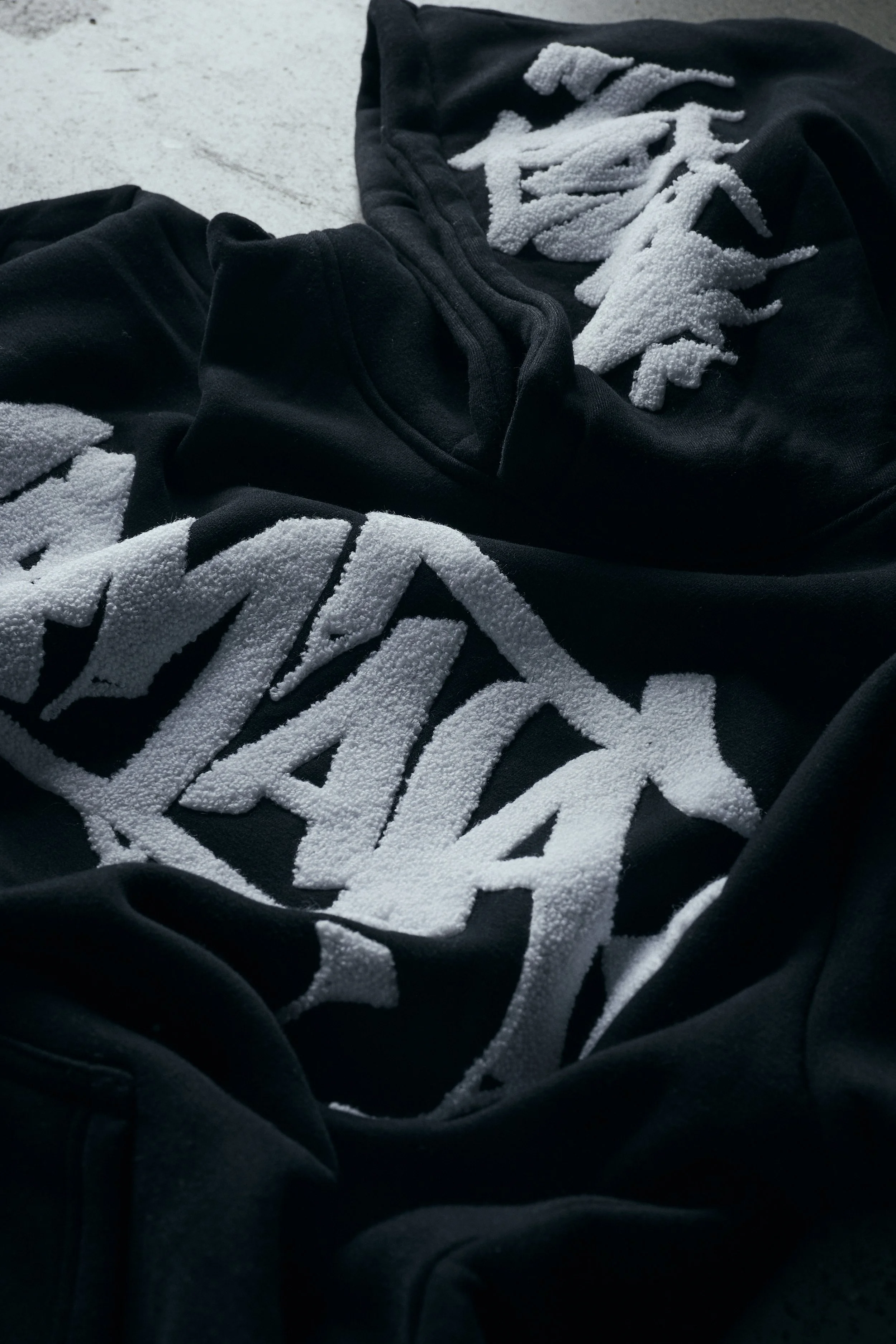 Close-up of black fabric with white textured design or lettering on it, lying on a concrete surface.