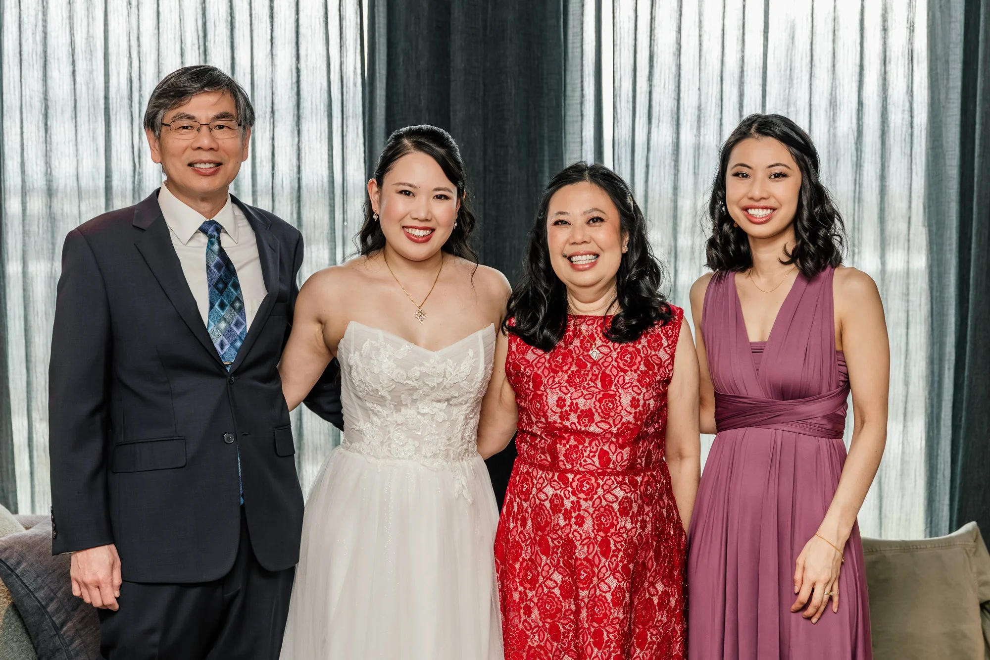 Group of four people standing together indoors, with a man in a suit and women in formal dresses, smiling at the camera.