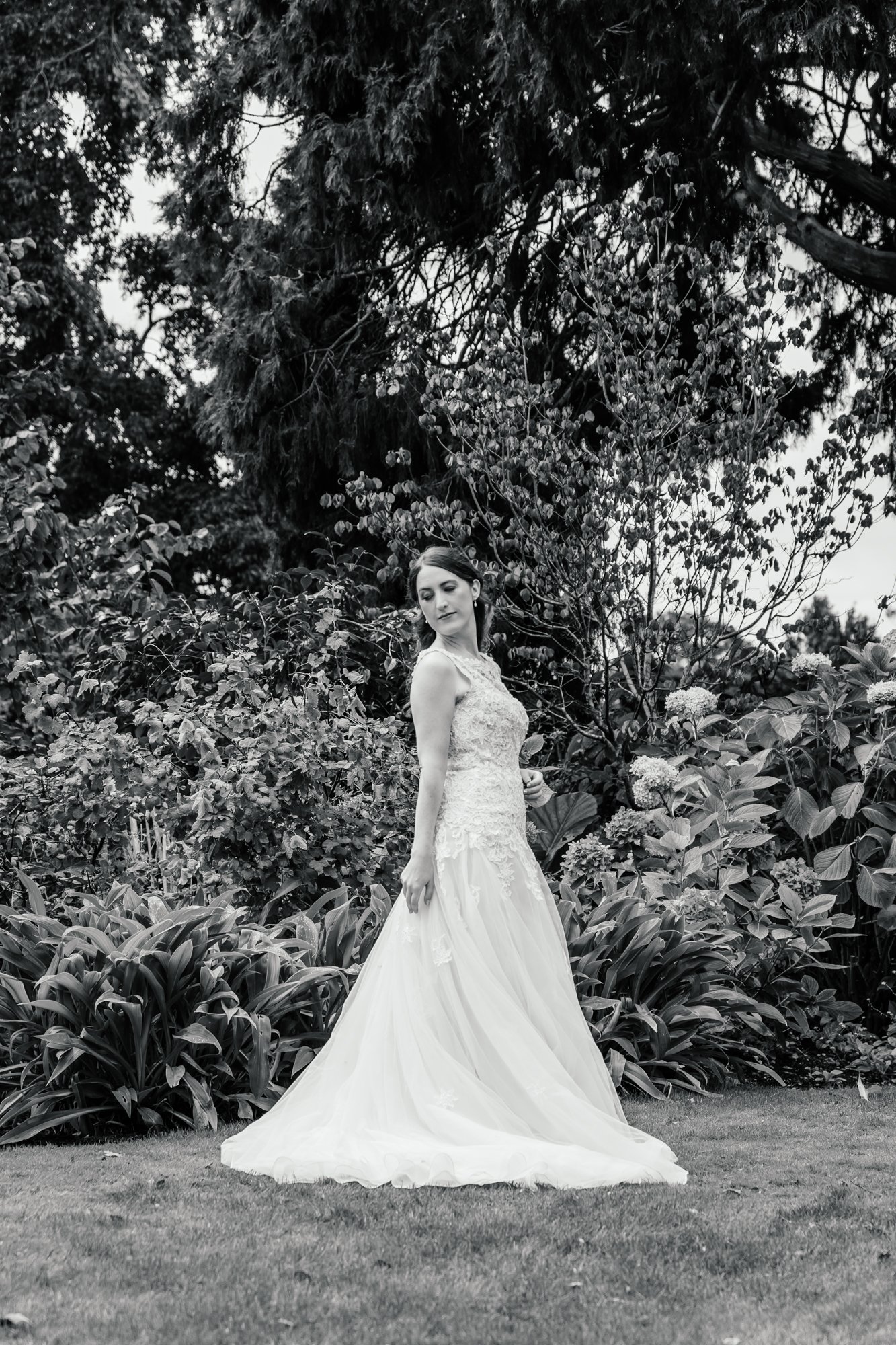A woman in a wedding dress standing in a garden with lush plants and trees in the background.