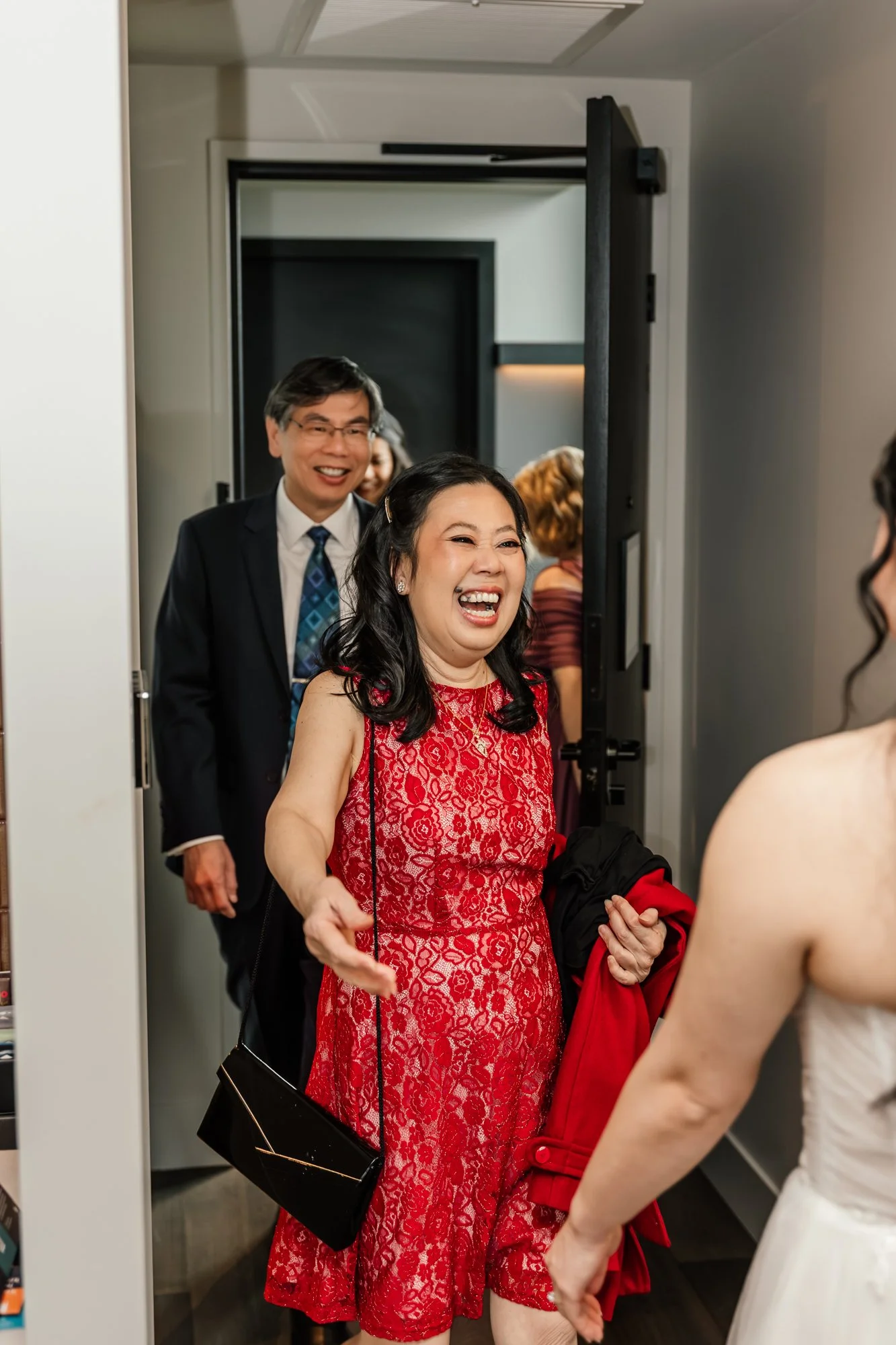 People dressed in formal attire smiling and interacting in a reception area, with a woman in a red lace dress at the center and others in the background.