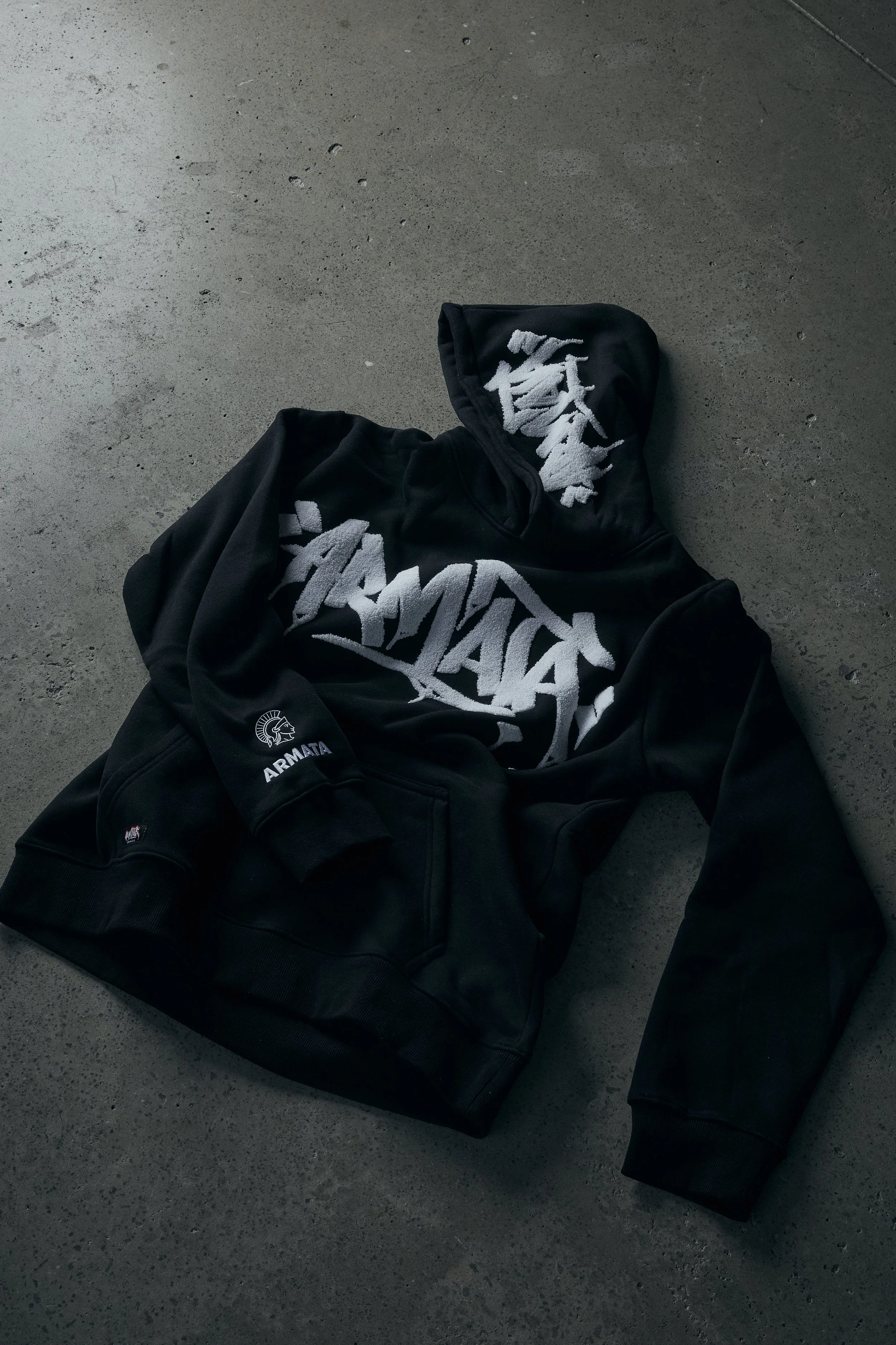 A black jacket with the words 'ARMATA' and an emblem on the left sleeve, lying on a concrete floor.