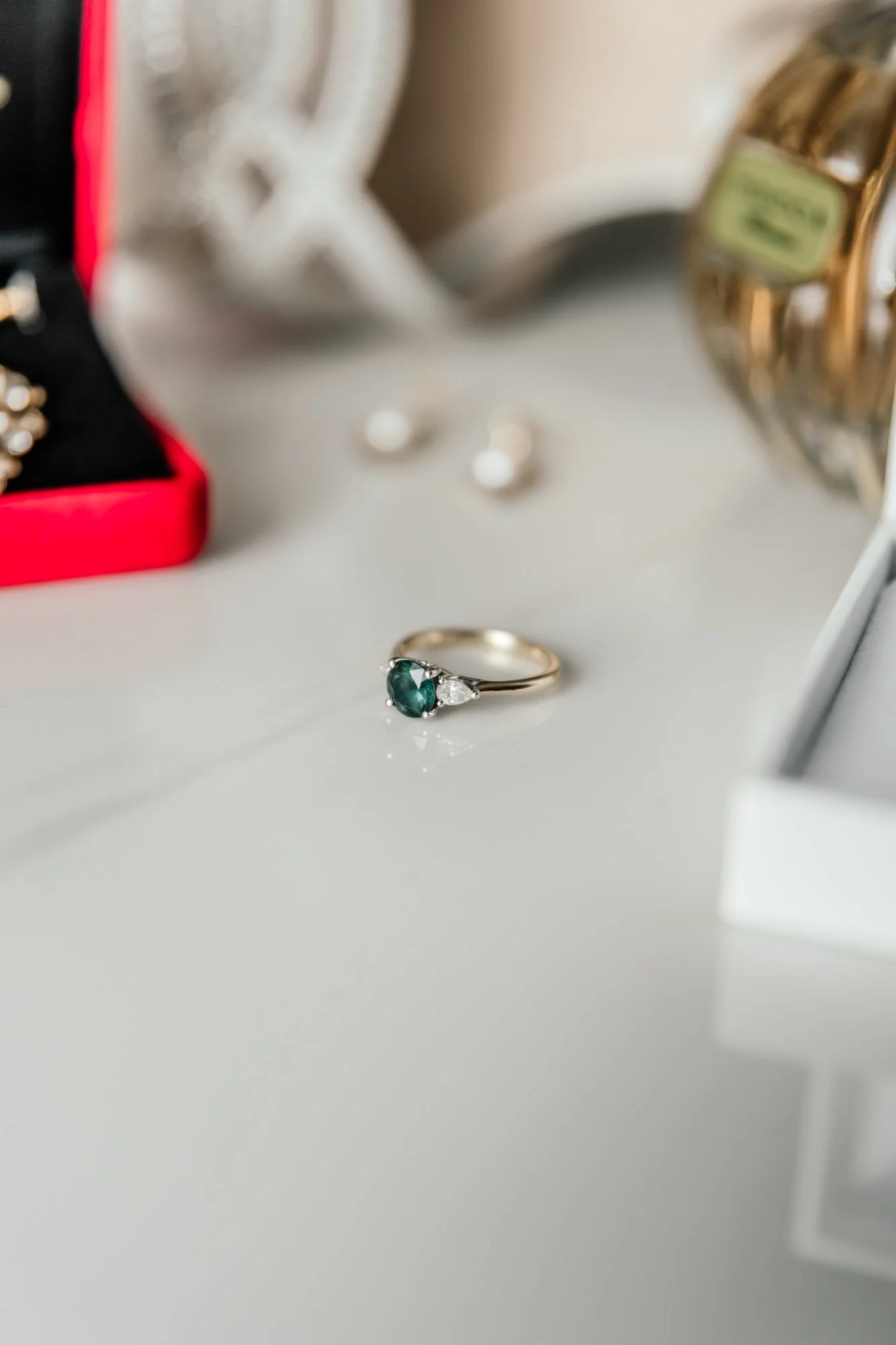 Close-up of a silver ring with a green gemstone, with blurred jewelry and a jewelry box in the background.
