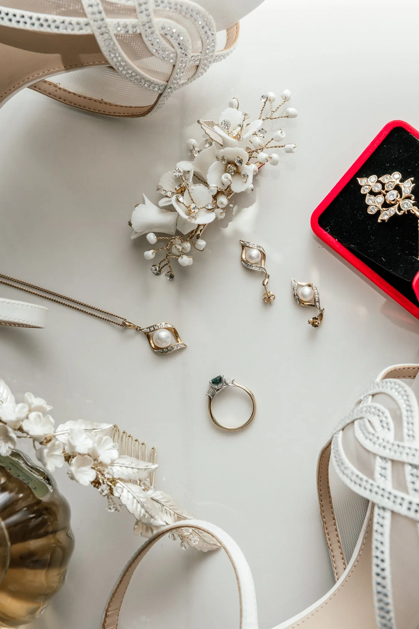 A collection of jewelry including earrings, necklaces, and bracelets, along with decorative shoes and a vase with white flowers, arranged on a white surface.