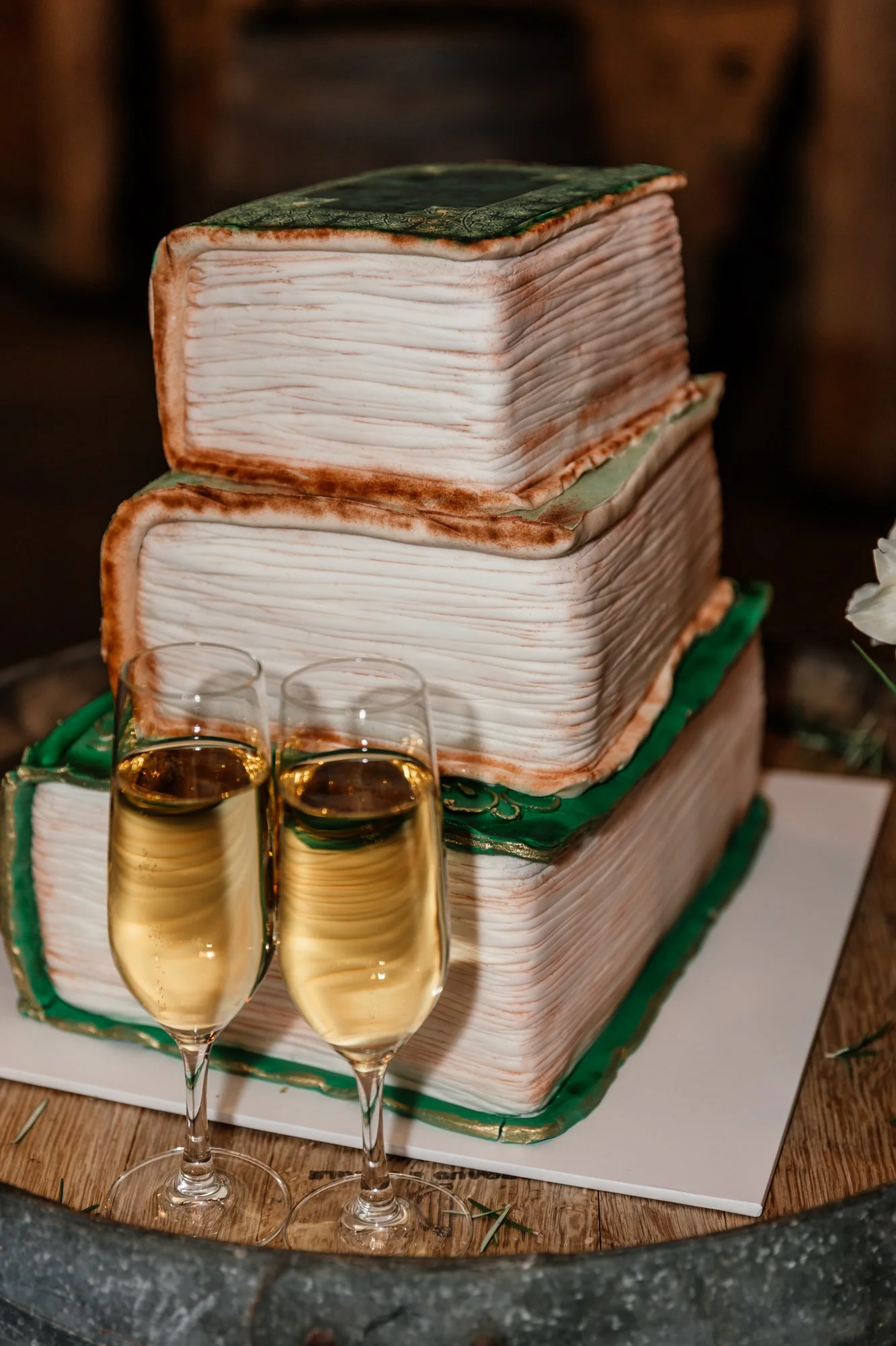A cake designed to look like a vintage book, decorated with green and gold accents, with three glasses of champagne in front.