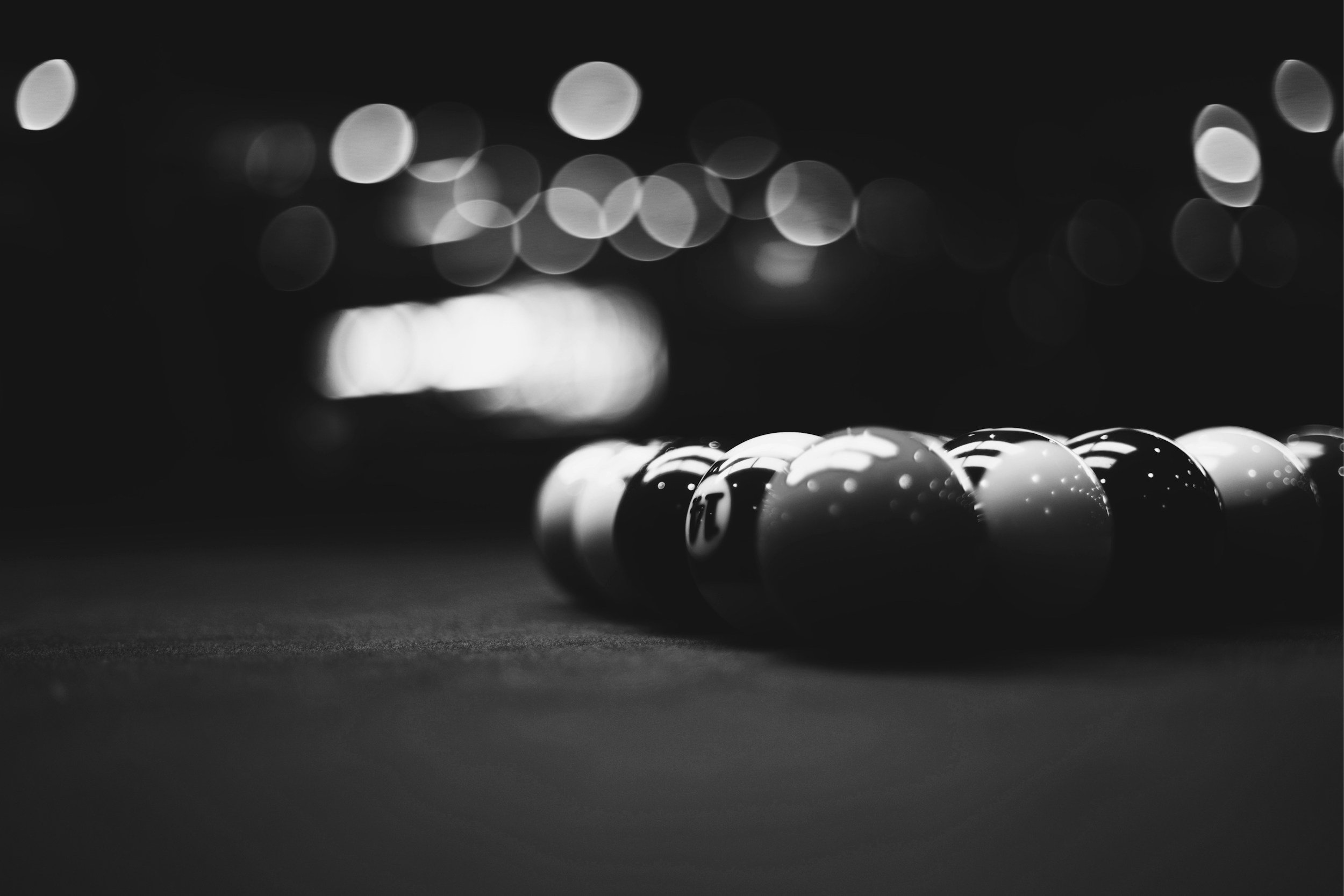 Black and white photo of pool balls arranged in a close line on a pool table, with blurred headlights or lights in the background.