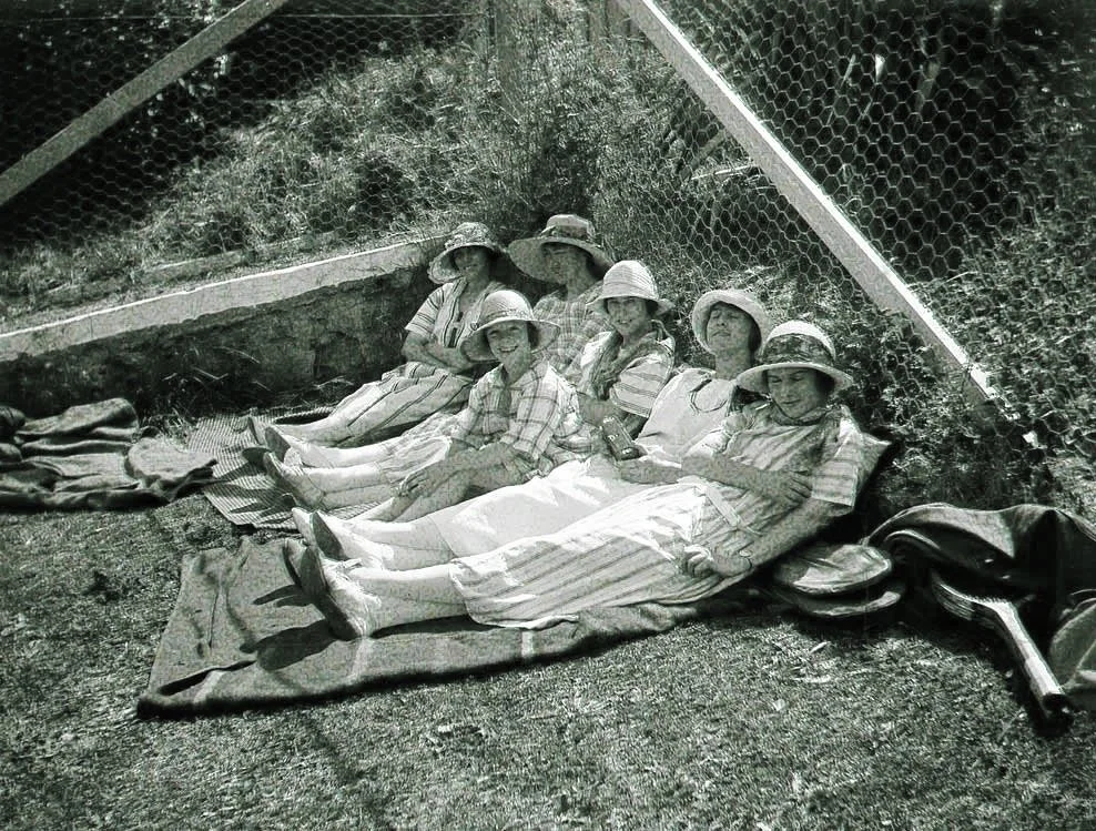 vintage image of five young ladies relaxing in the shade in the corner of a tennis court, leaning against an old fence that looks like some of the fences on the mornington peninsula