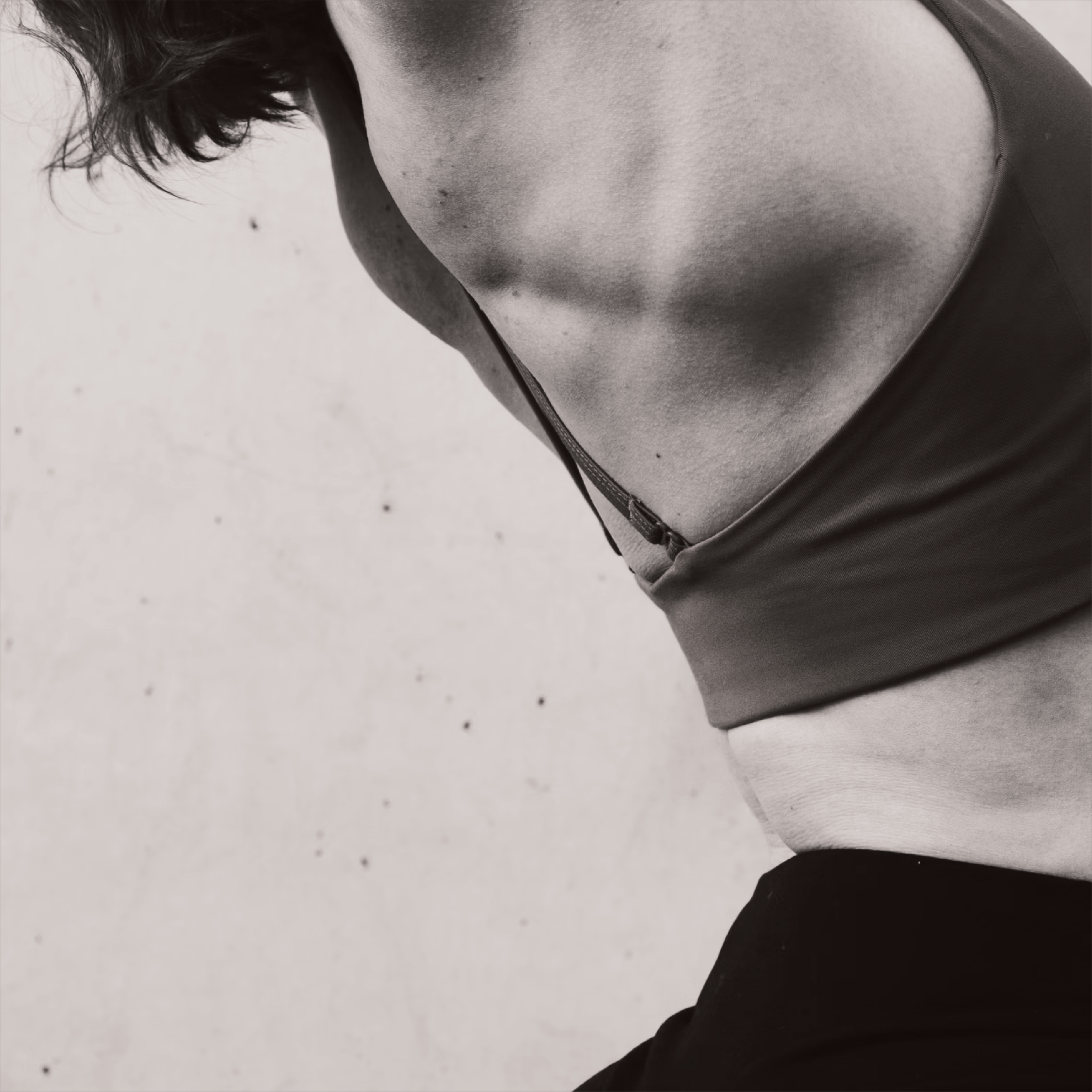 Black and white close-up of a person's torso in an athletic pose, wearing a sports top and pants, highlighting muscle definition.