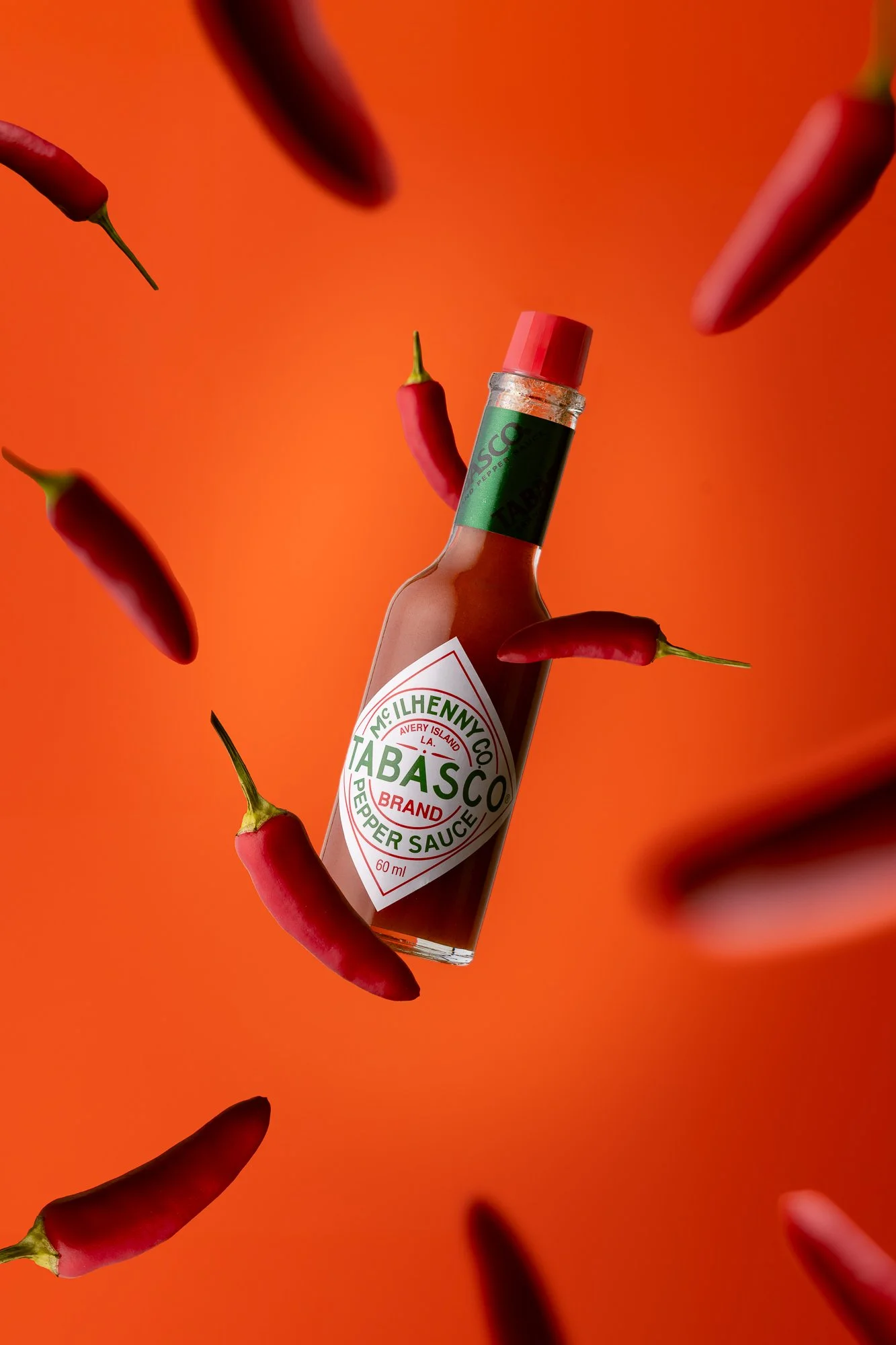 Flasche Tabasco Soße ist in der Mitte, umgeben von roten Chilischoten auf einem orangefarbenen Hintergrund.