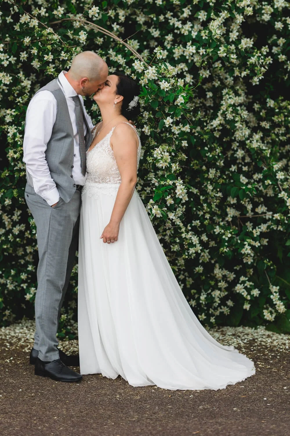 Ein Hochzeitspaar küsst sich vor einem Hintergrund aus blühenden weißen Blumen.