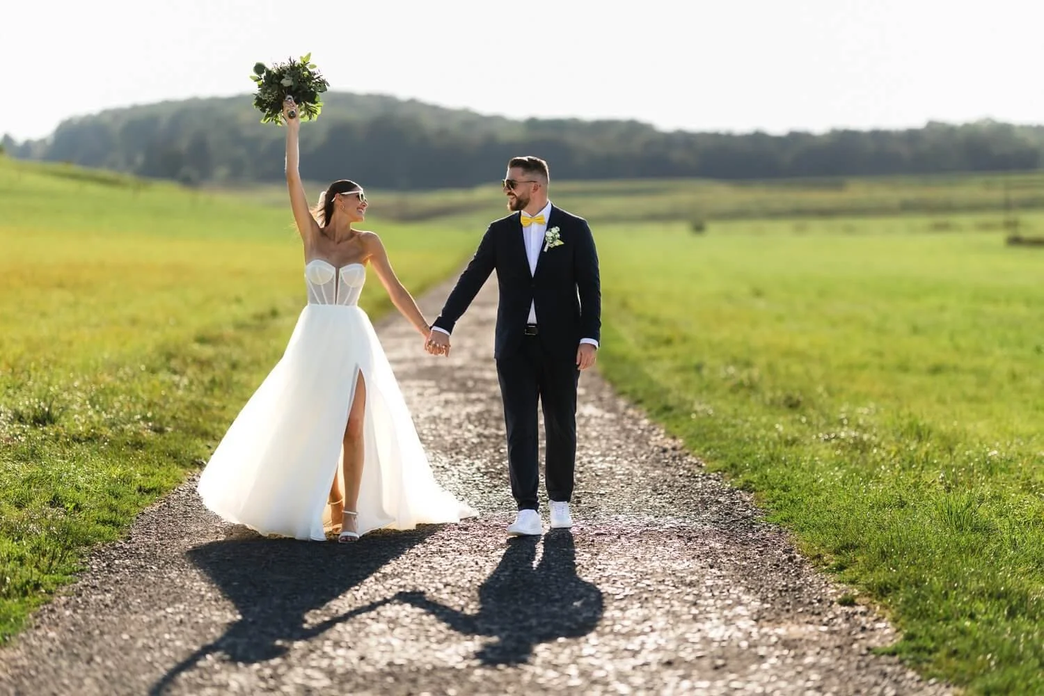 Brautpaar läuft lächelnd Hand in Hand und die Braut hält ihren Brautstrauß in die Luft