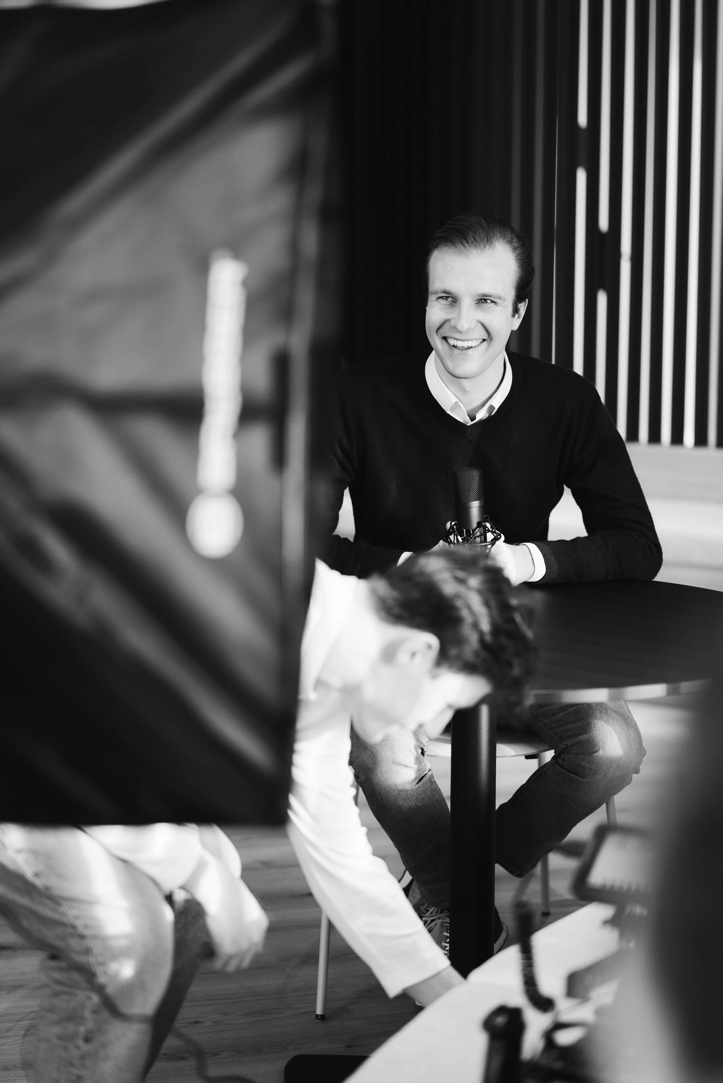 Man met luisterend oor en microfoon, lachend, tijdens interview, in professionele setting.