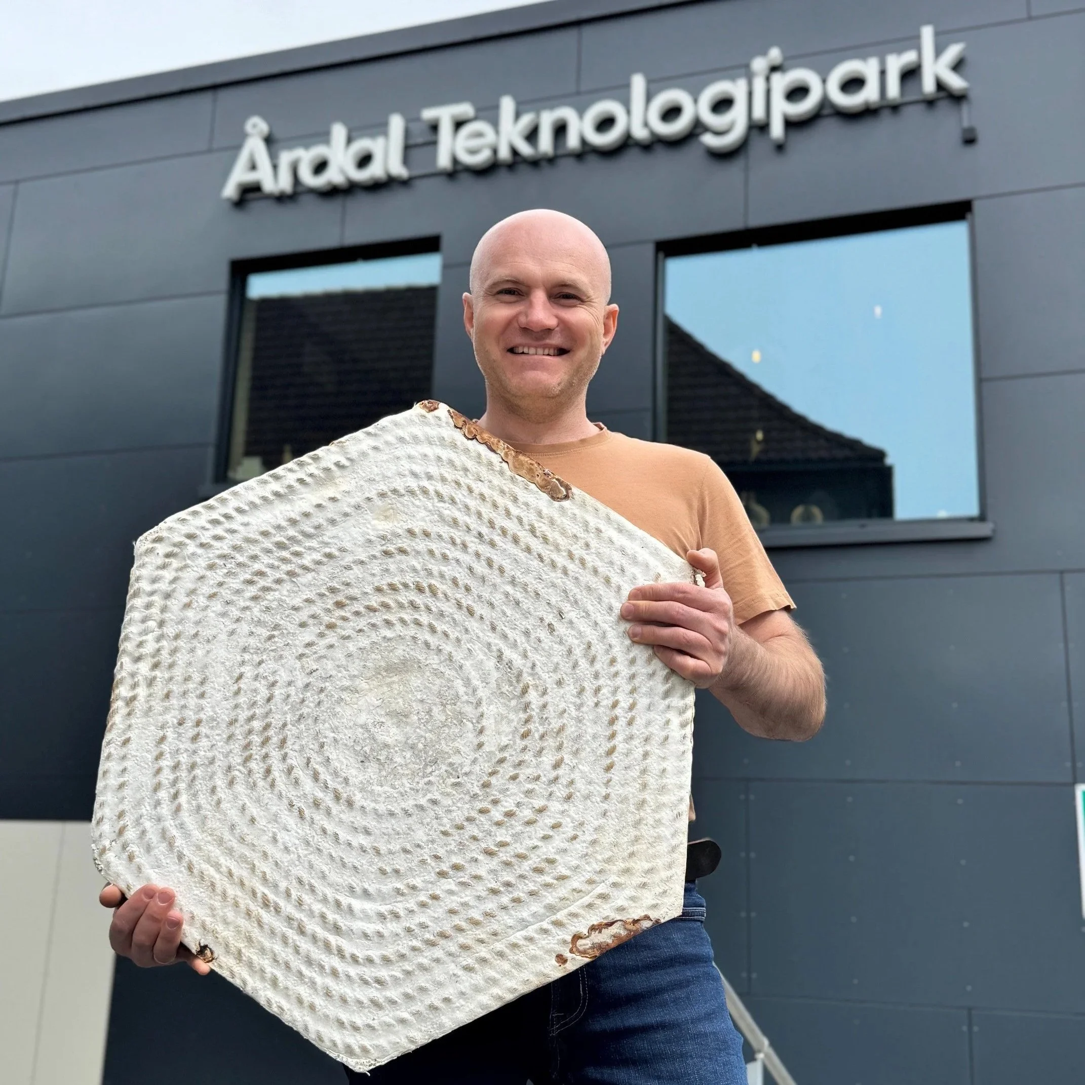 Person som holder en stor risselakt stykk av brød foran en bygning med skiltet "Ardal Teknologipark".