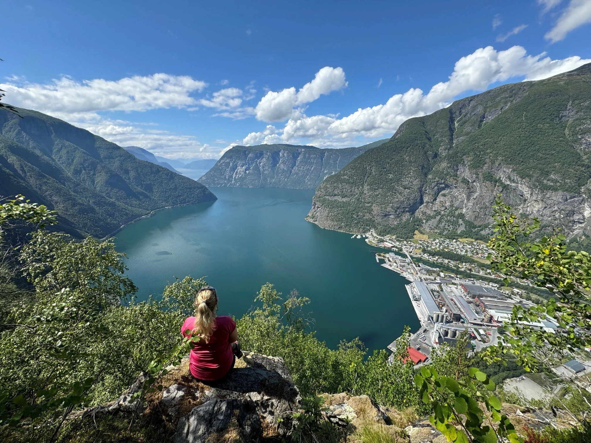 Kvinne med blå jakke ser på fjord og fjell fra utkikkspunkt.