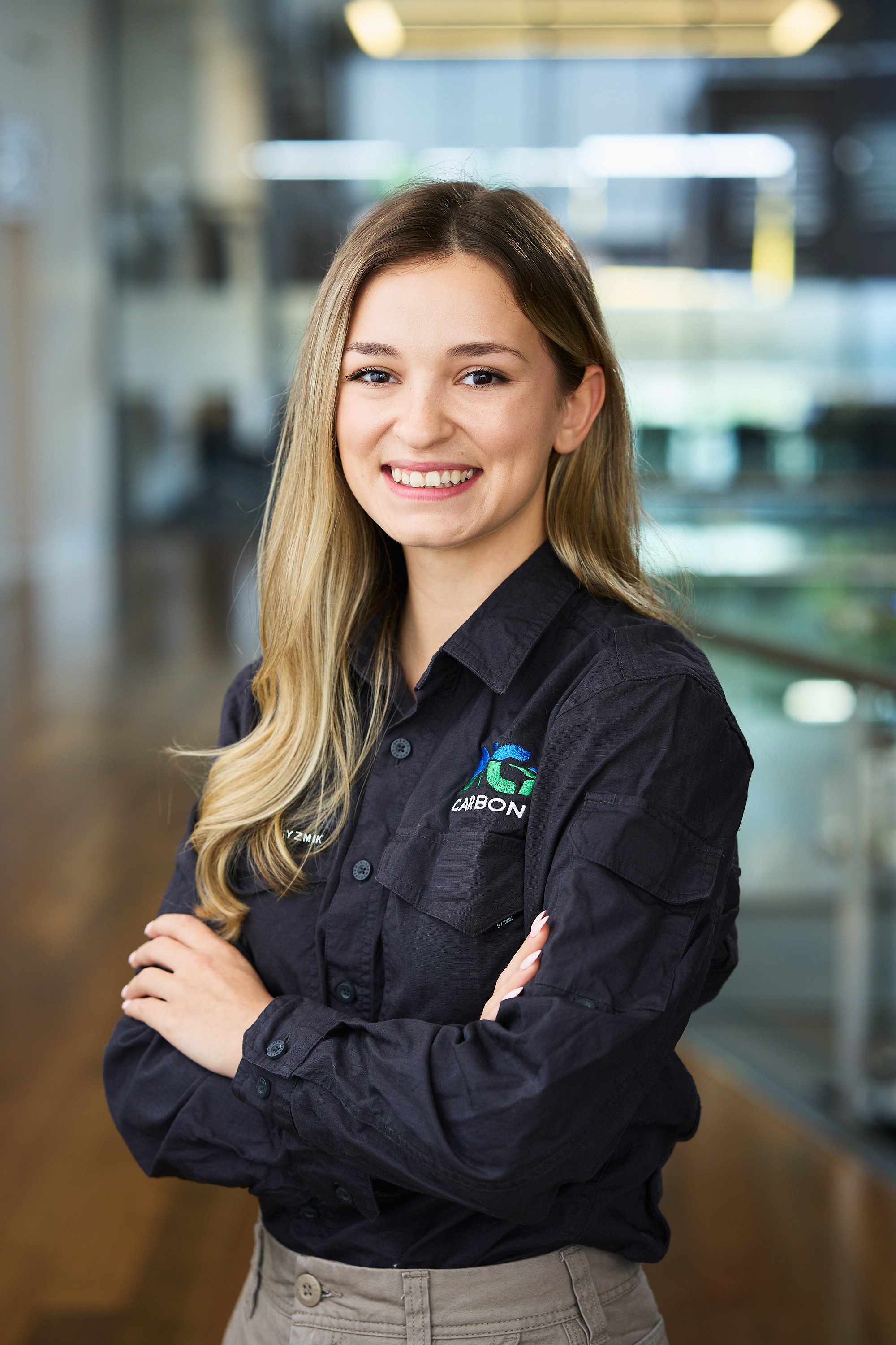 Smiling woman in a black shirt with company logo, standing indoors.