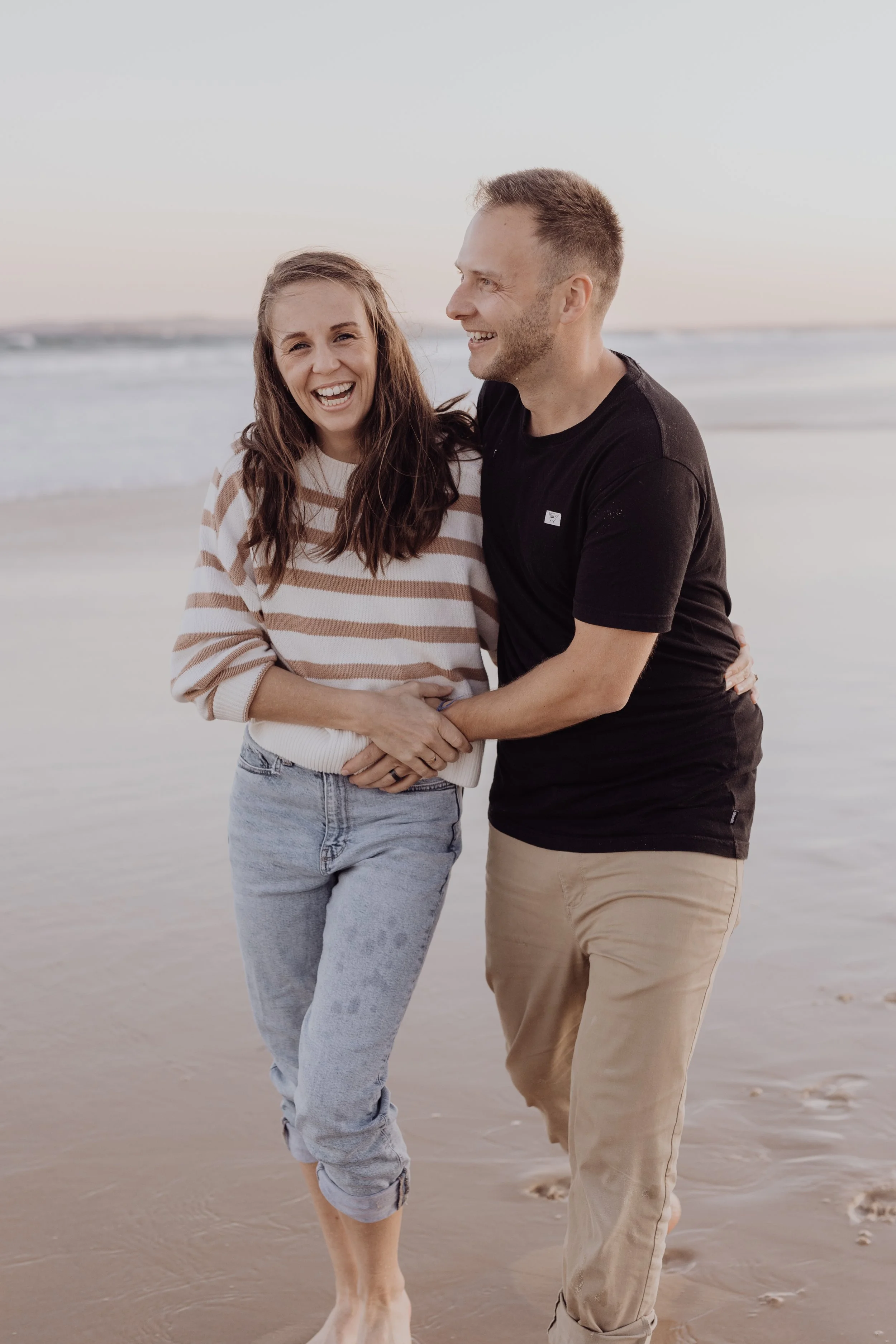 Couple laughing and walking on a beach.