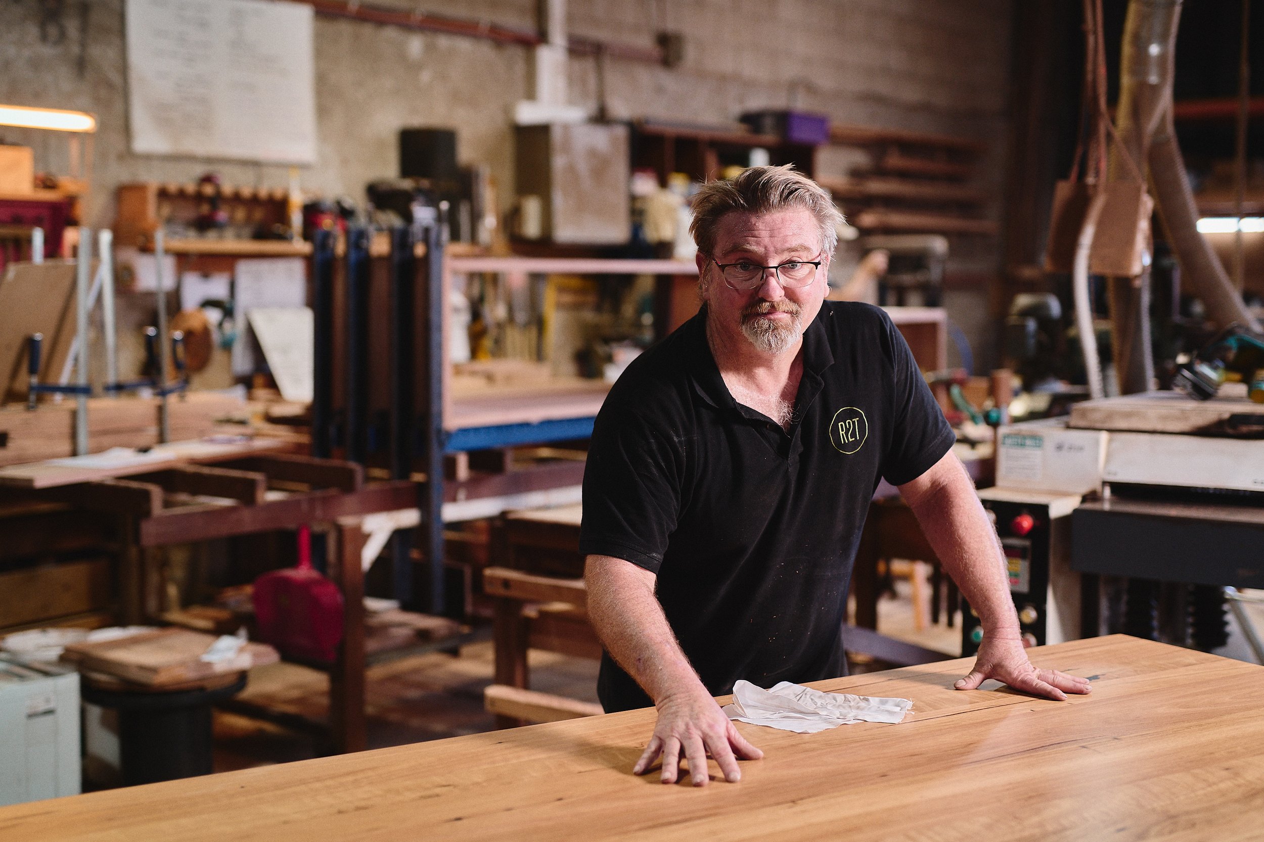 Man in a workshop with woodworking tools and furniture.