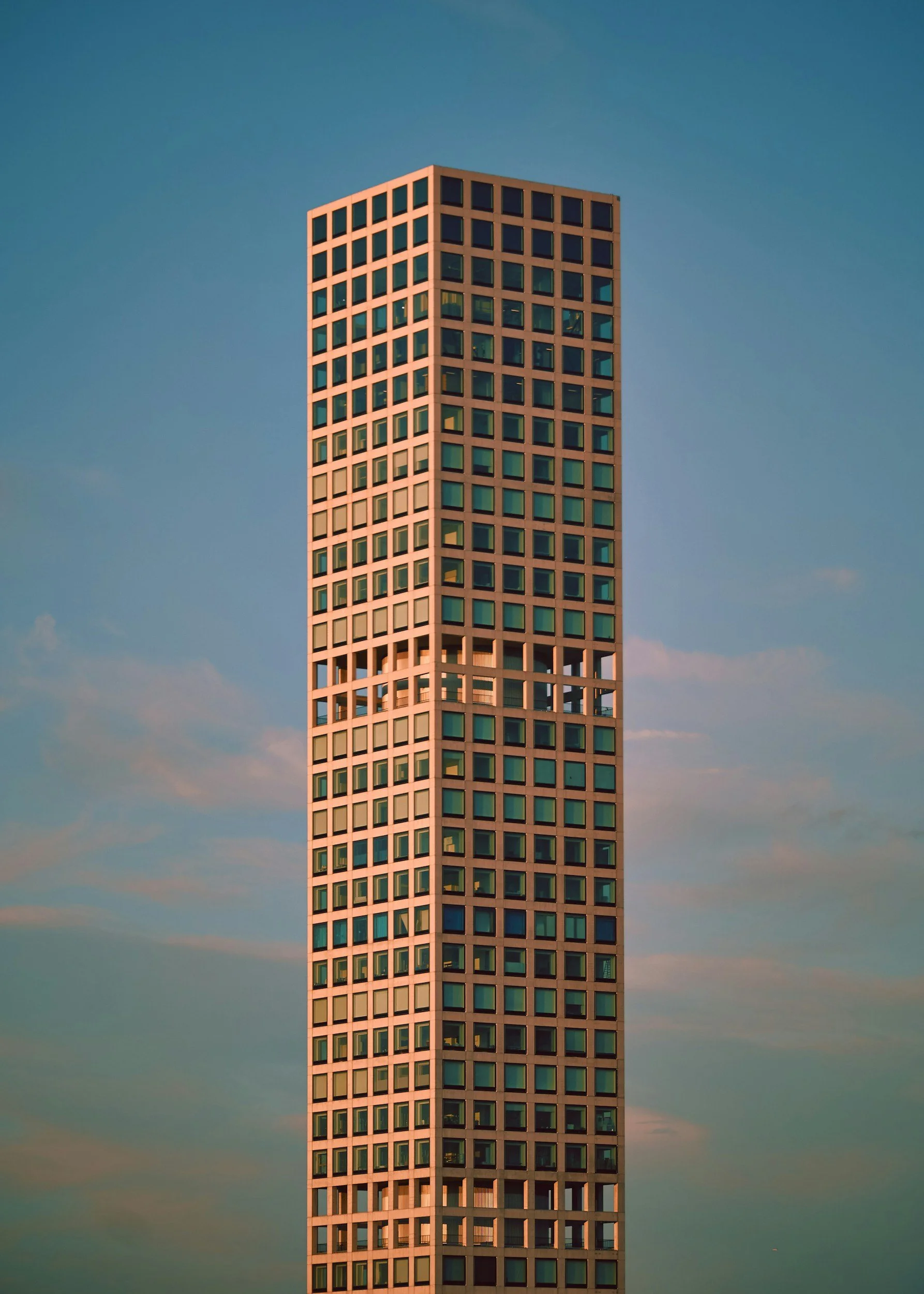 Tall building with a grid of square windows, set against a blue sky with scattered clouds.
