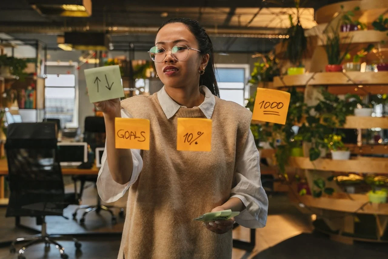 A business owner arranging sticky notes for goals and targets on a glass wall