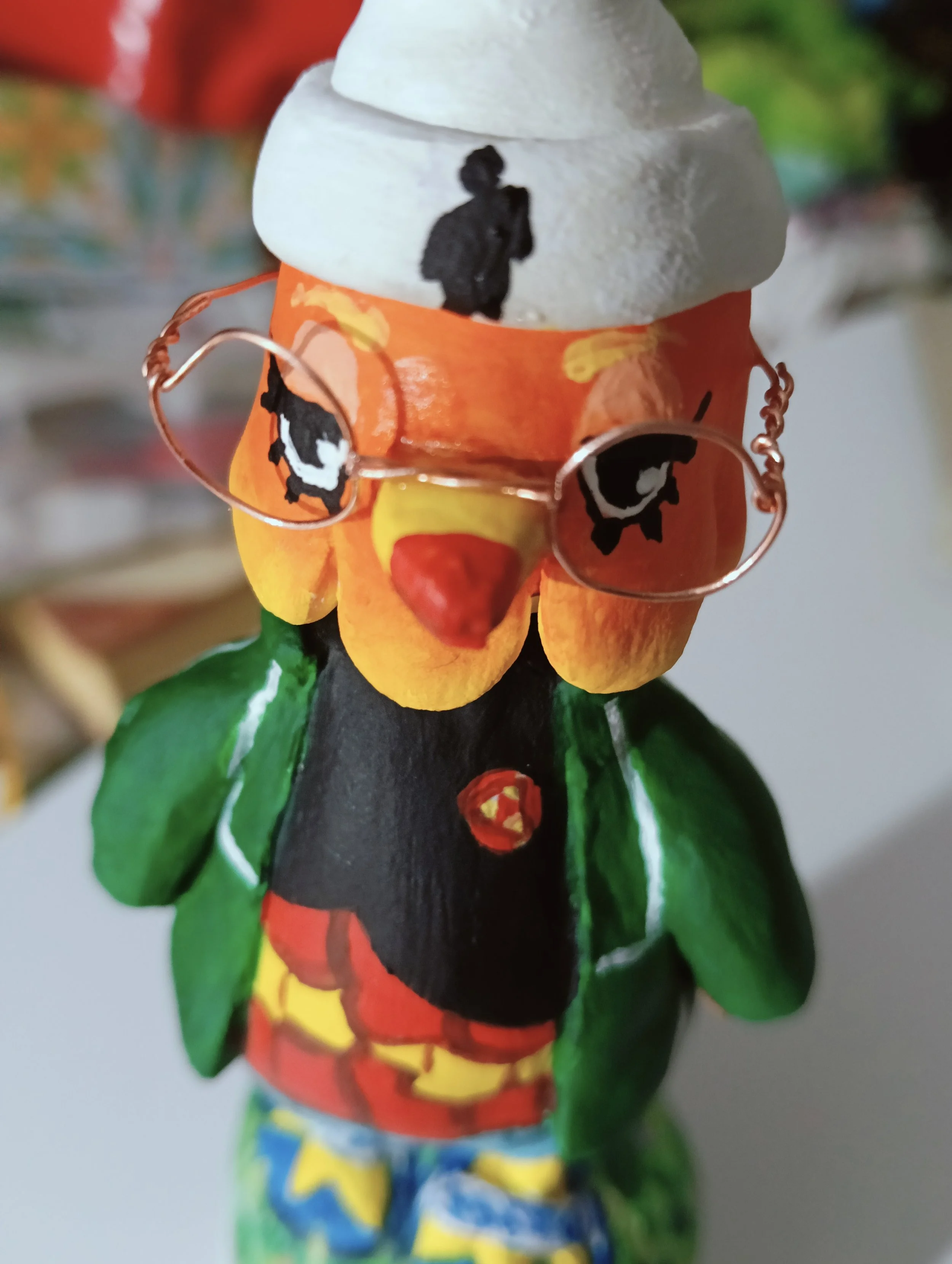 A handcrafted figurine of a woman in a traditional dress with painted facial features, holding a small object, with a background of colorful blurred objects.
