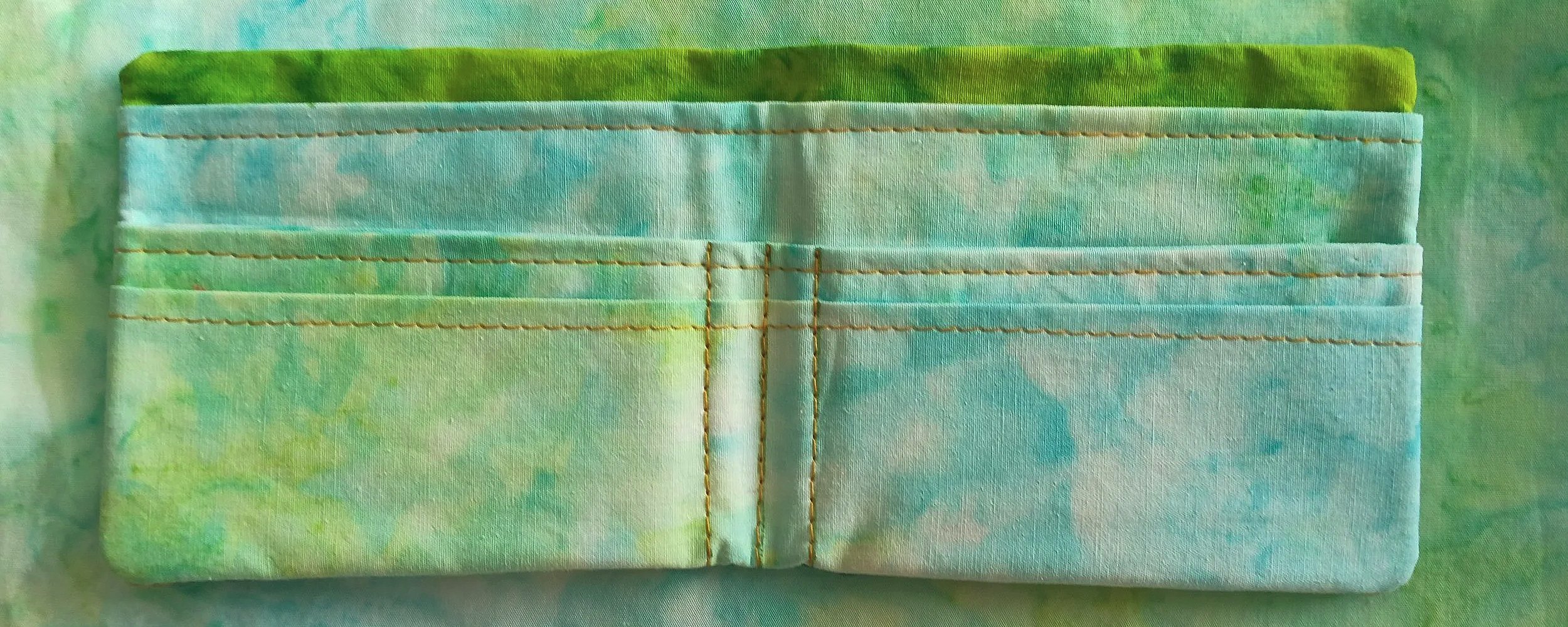 Close-up of a fabric wallet with multiple card slots, featuring a tie-dye pattern in shades of green, blue, and white.