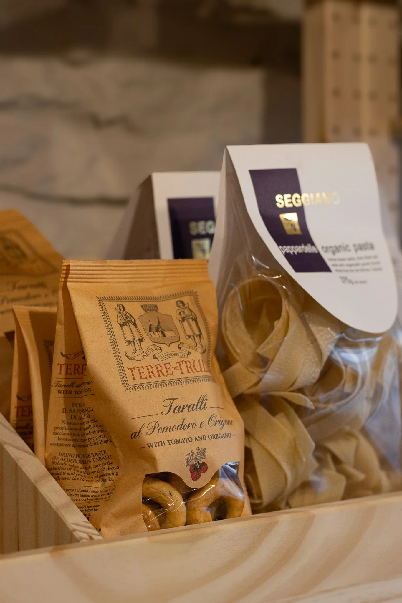Various packages of Italian pasta, including Taralli with tomato and oregano, displayed in a wooden basket. The Cotswold Farm. 