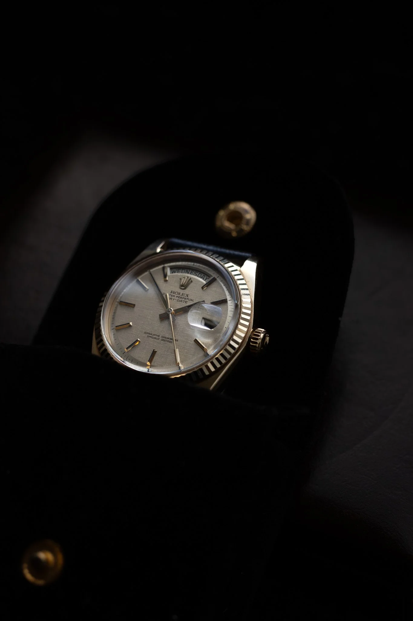 Close-up of a Rolex watch with a silver face and gold accents, displayed inside a black box with a folded lid. Aurmont. Watches.