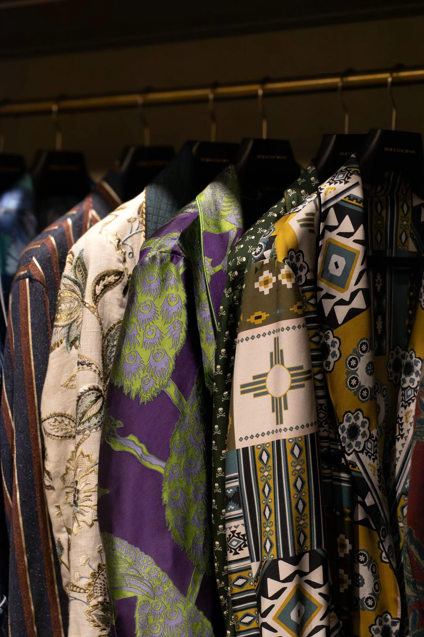 Clothing with colorful, patterned fabrics hanging on a rack. New & Lingwood.