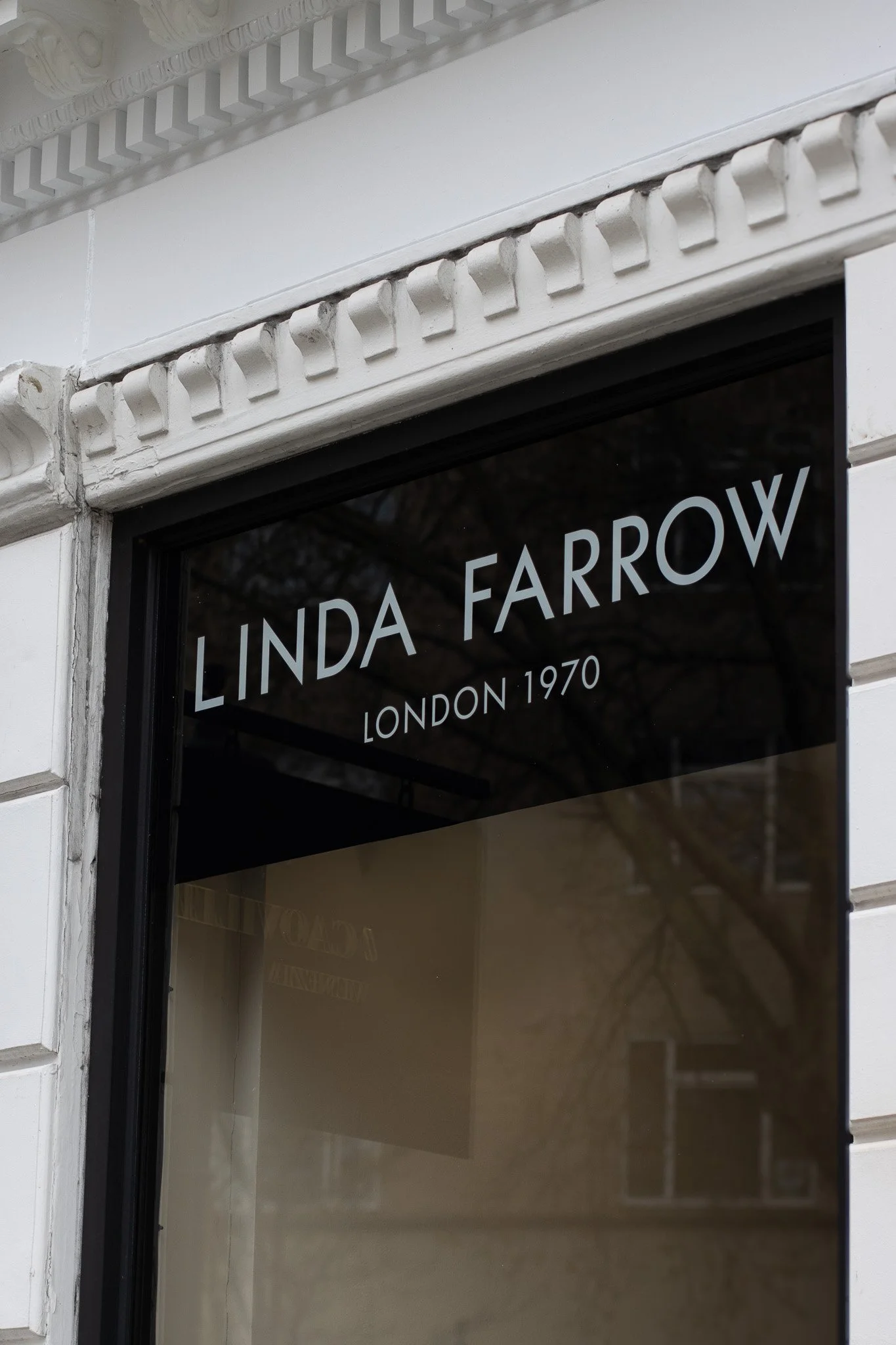 Close-up of a shop window with white lettering that reads 'LINDA FARROW LONDON 1970'. The architectural details include decorative molding on the building's corner. Linda Farrow.